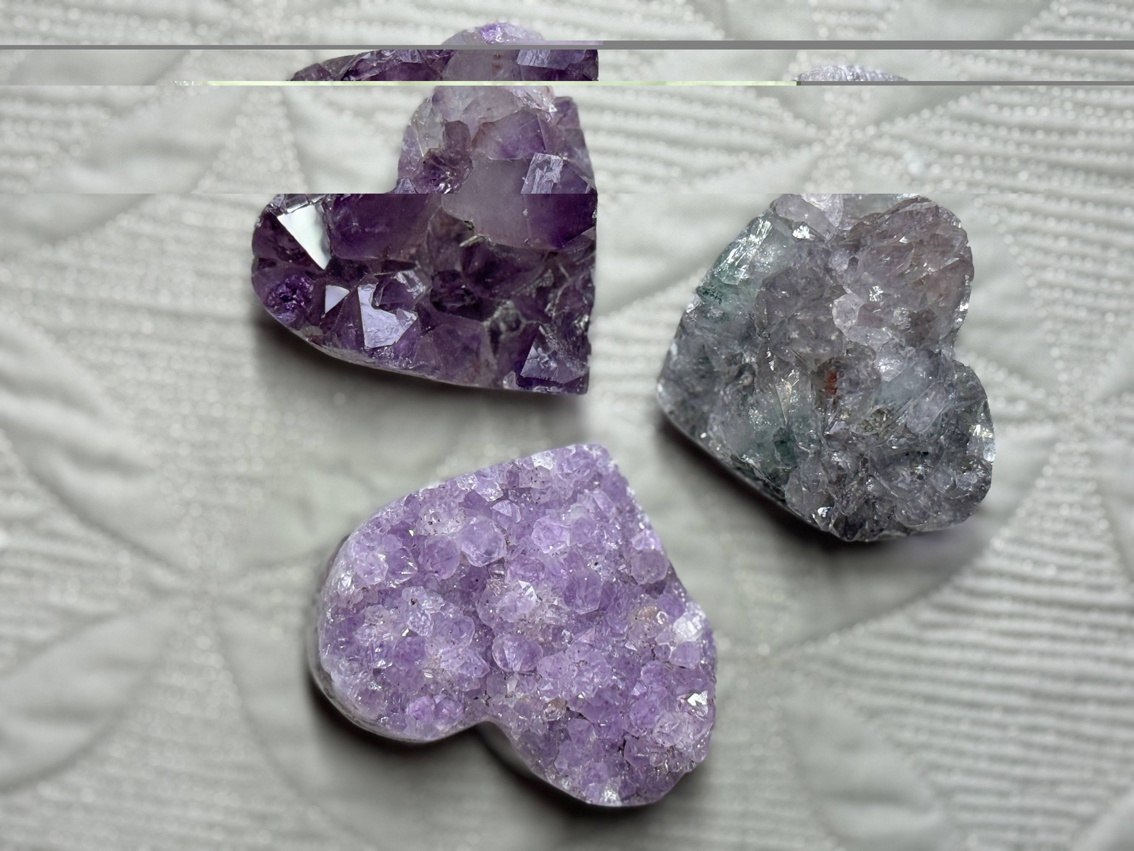 x3 different coloured purple amethyst hearts lying on a grey background