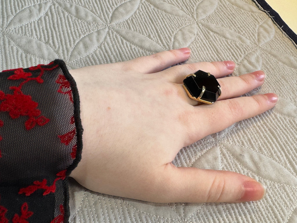Hand wearing a black ring on a textured fabric background