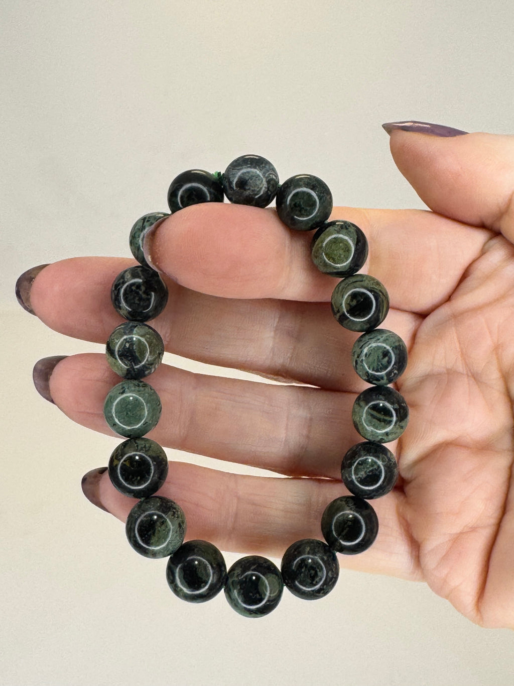 Hand holding a black beaded bracelet against a neutral background