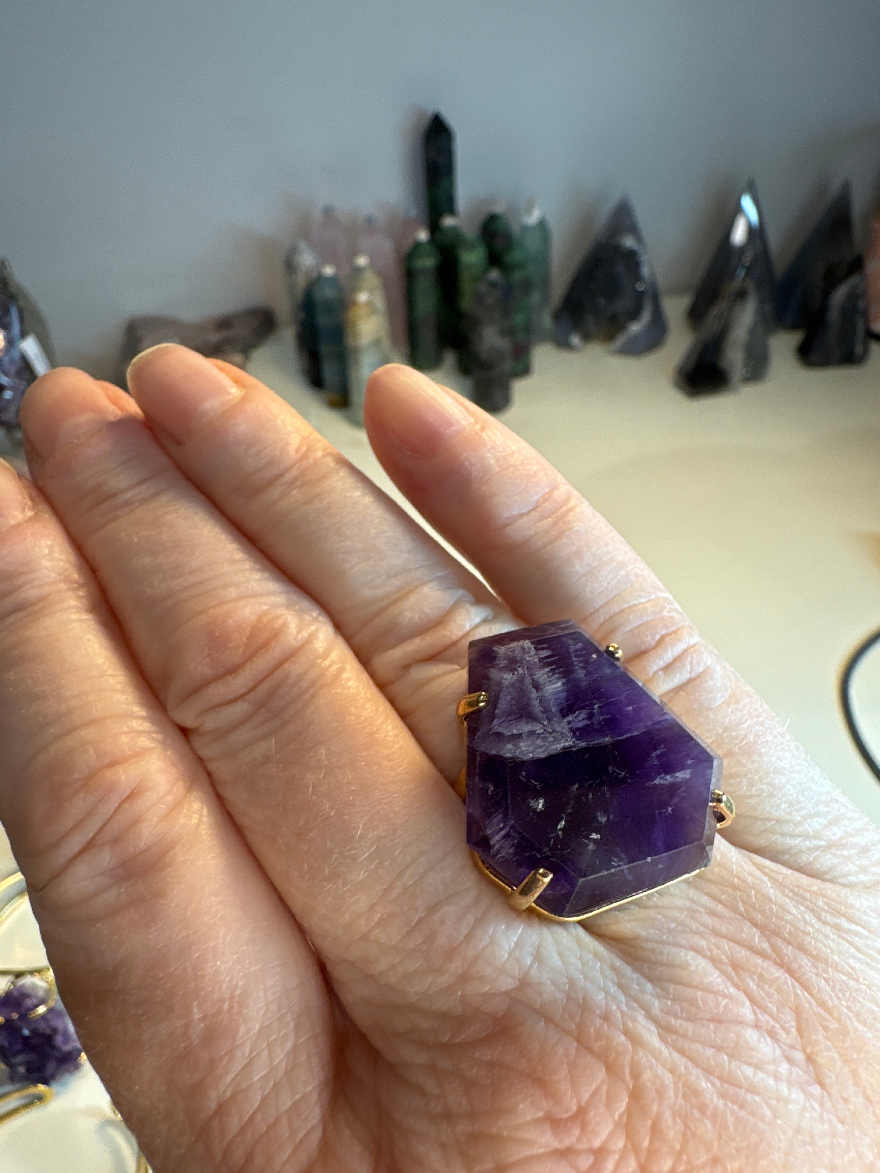 Hand wearing a purple crystal ring with a blurred background of crystals.