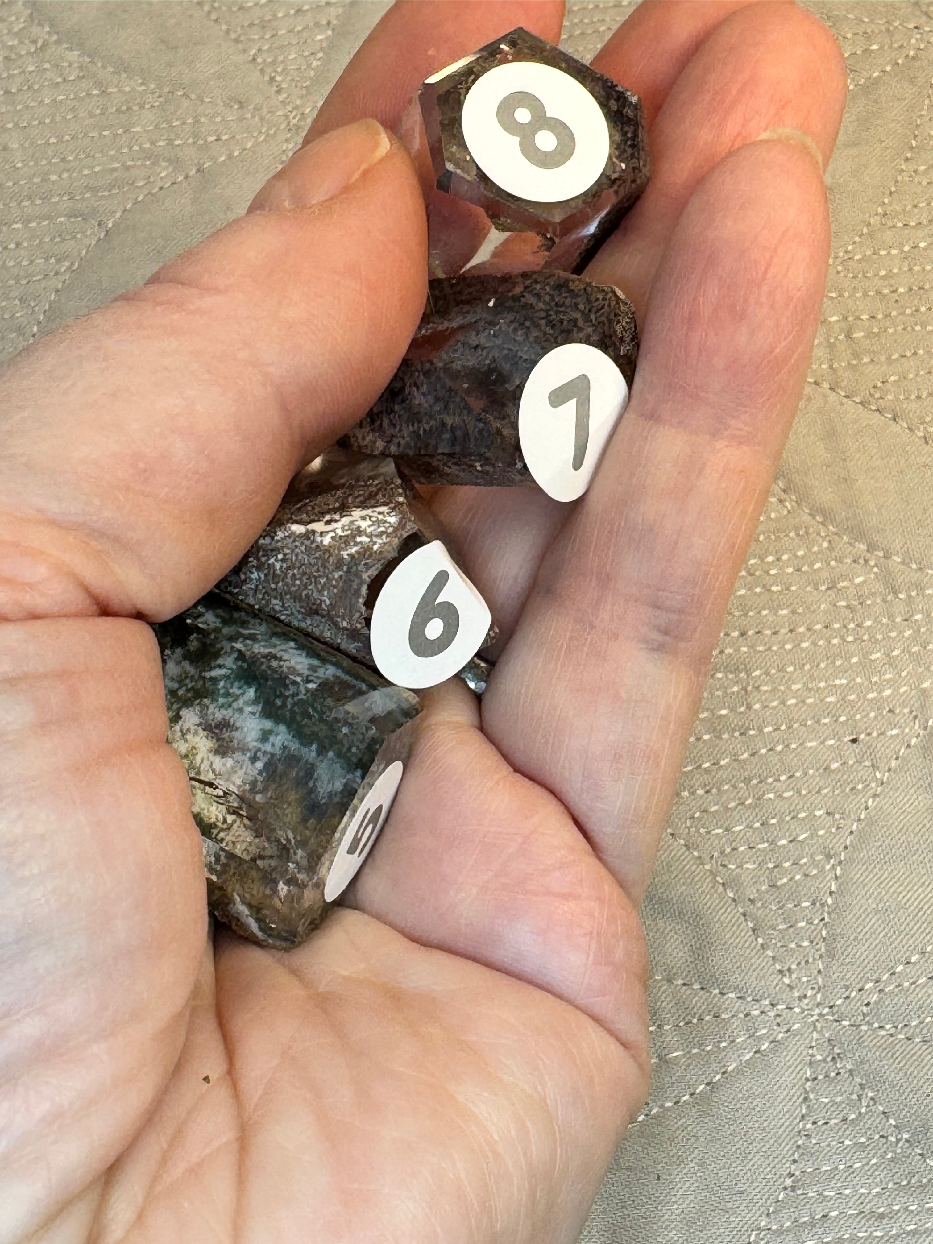Hand holding four hexagonal metal objects with numbered labels on a beige background