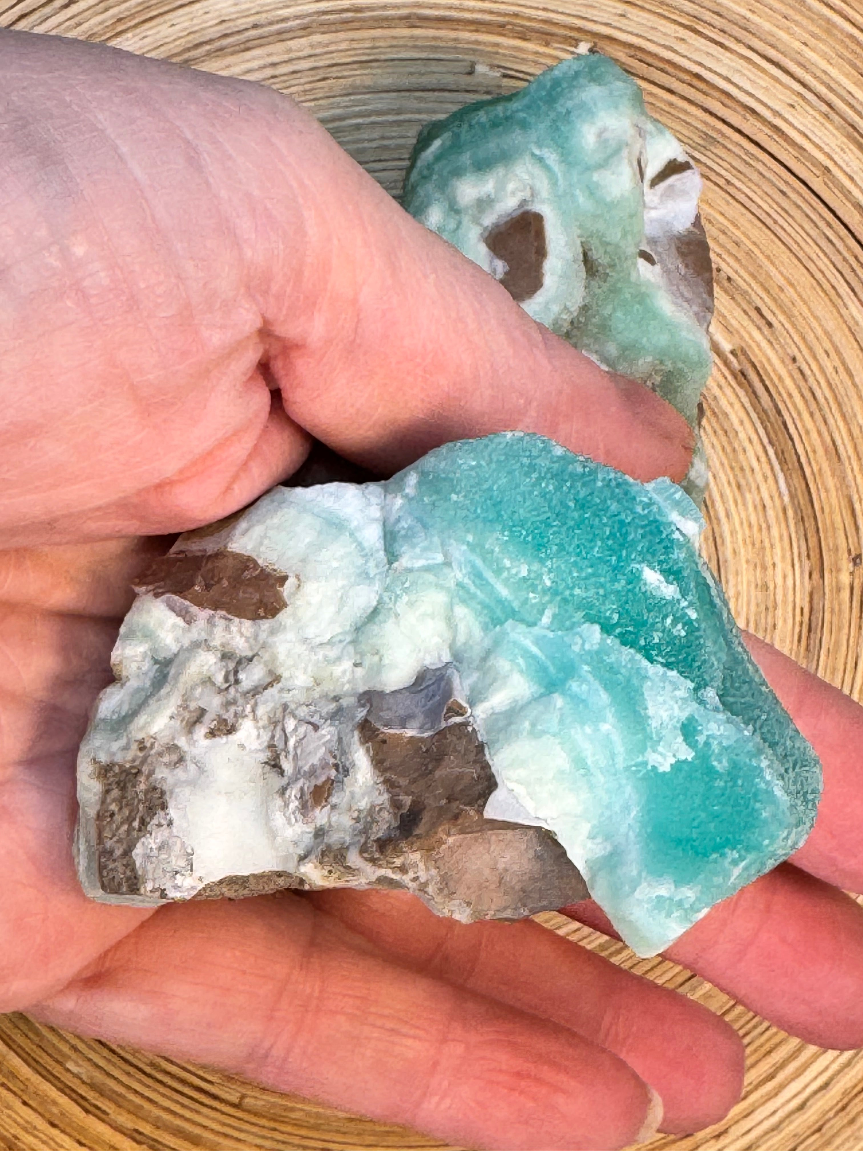 Hand holding a rough cut gemstone with a natural pattern on a wooden surface