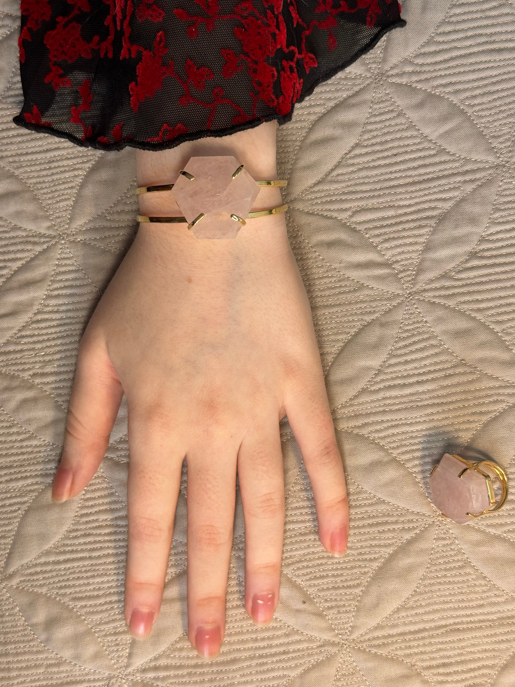 Hand wearing a gold bracelet on a textured beige surface