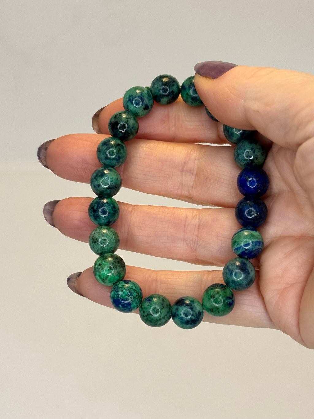 Hand wearing a green and blue beaded bracelet on a plain background