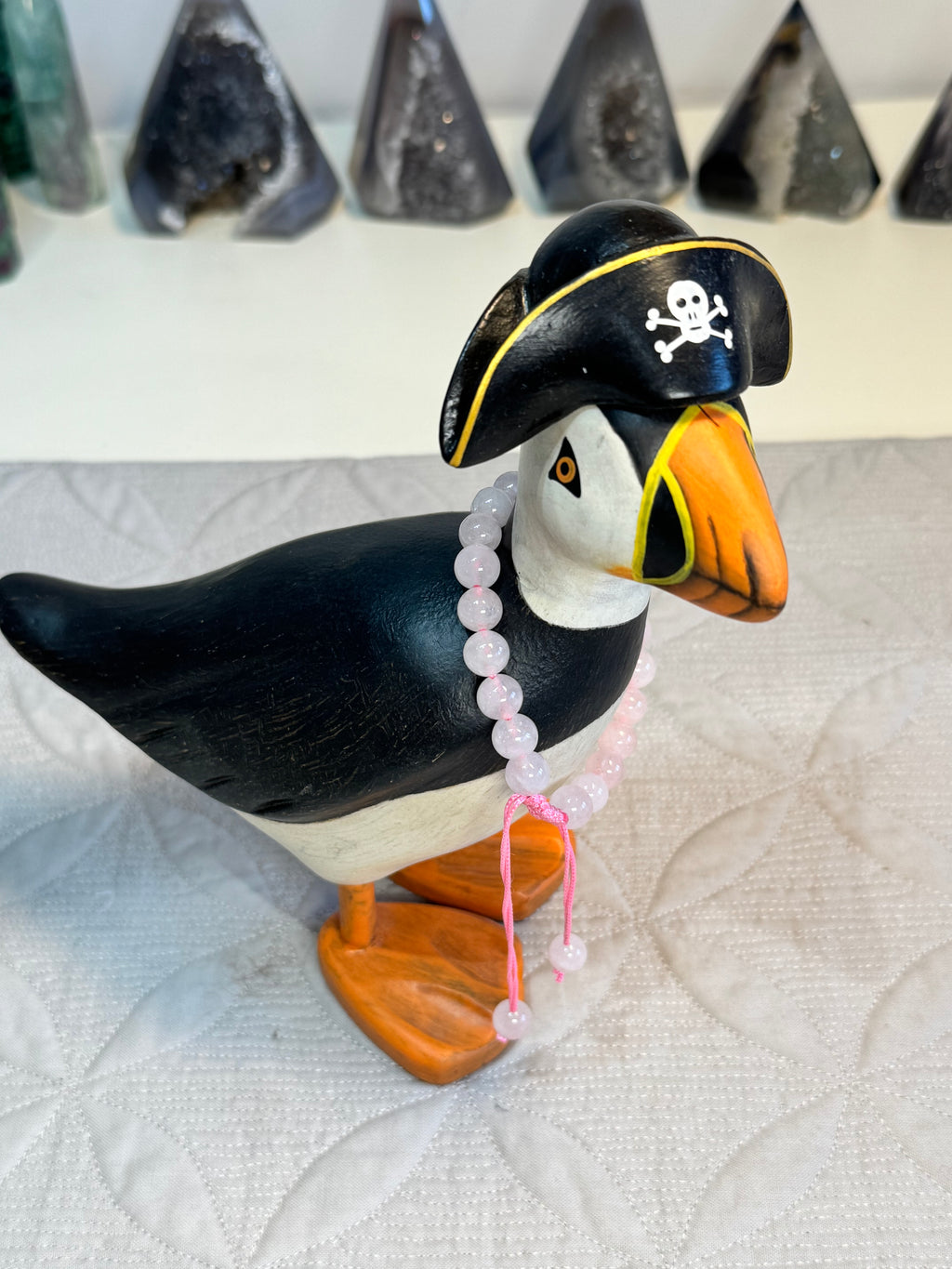 Puffin figurine wearing a pirate hat with a skull and crossbones on a textured white surface. with bracelet around its neck