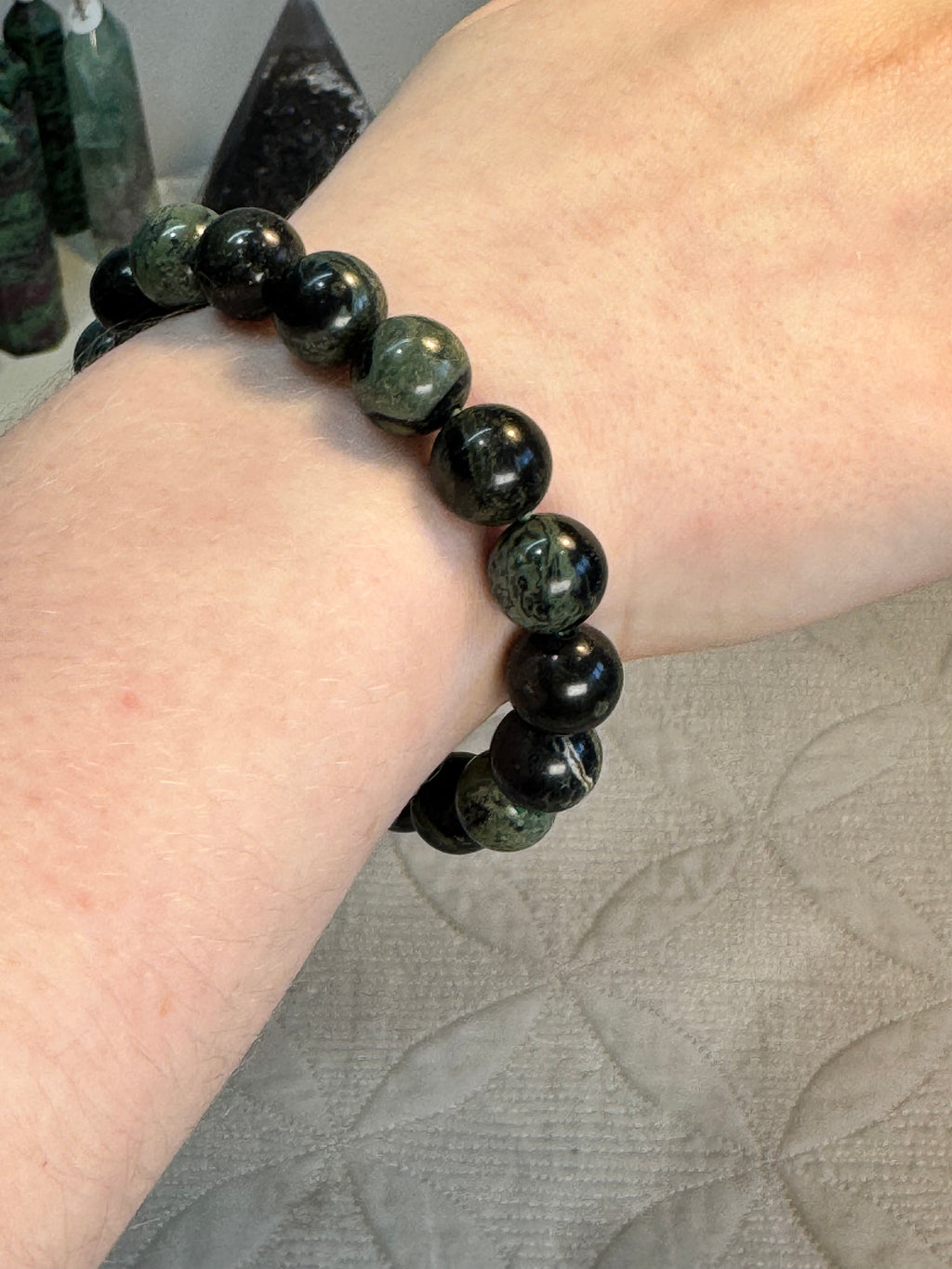 Black and green beaded bracelet on a wrist with a textured fabric background