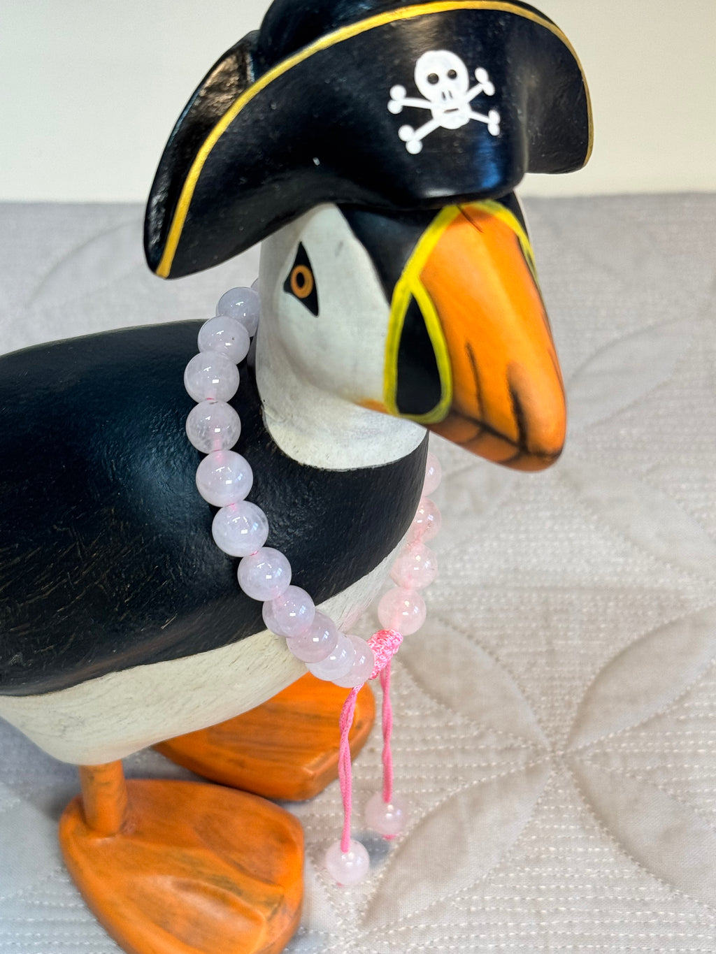 Puffin figurine wearing a pirate hat with a skull and crossbones on a textured white surface. with bracelet around its neck