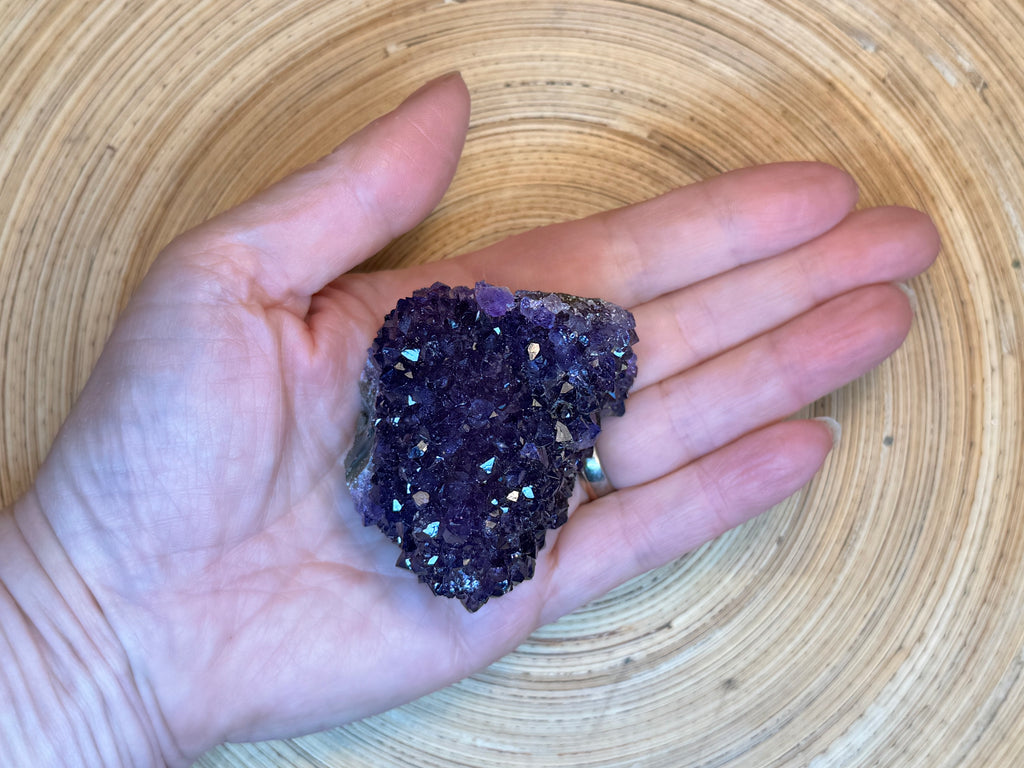 Hand holding a purple crystal against a wooden background