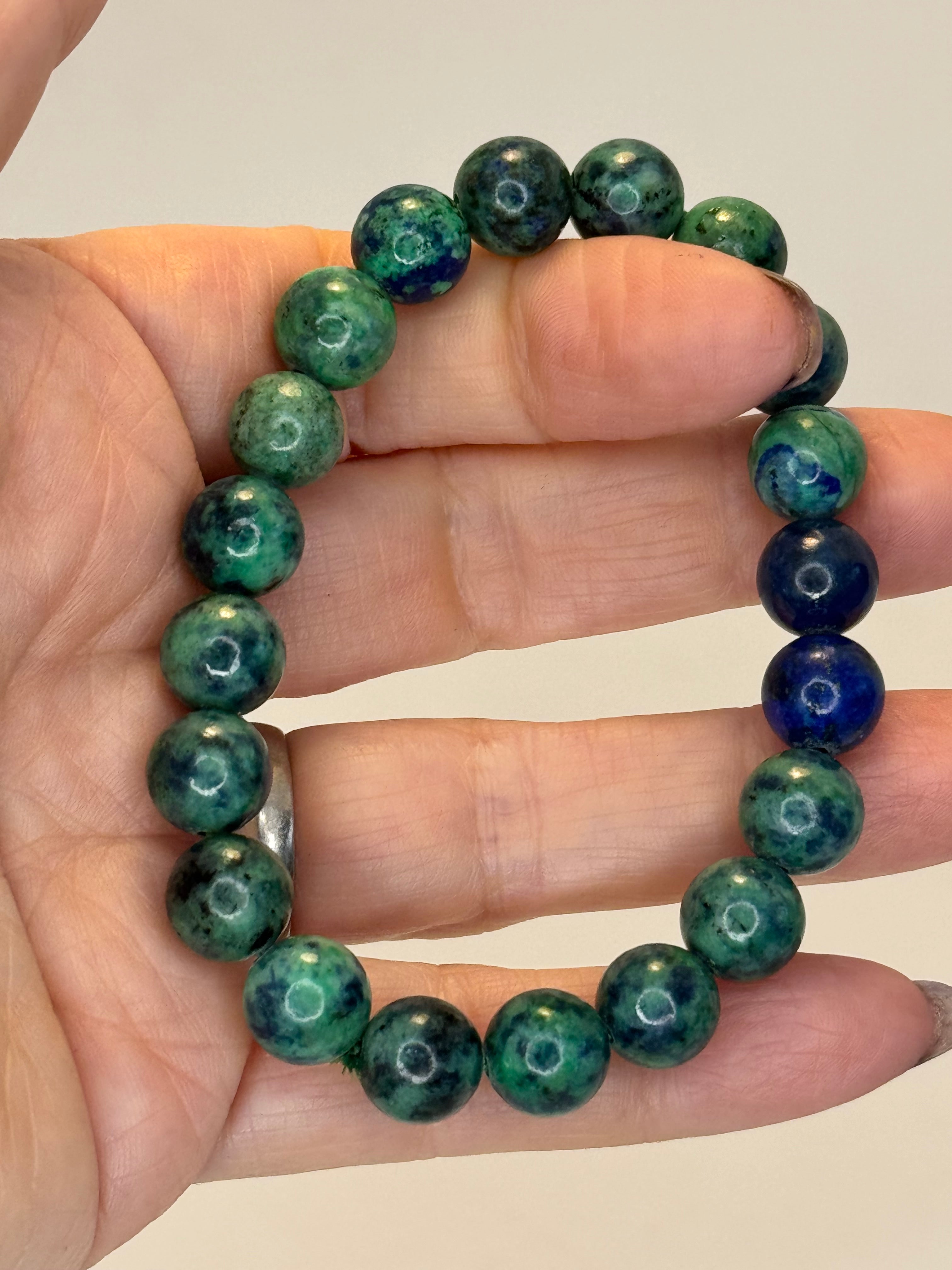Green and blue beaded bracelet on a hand against a plain background