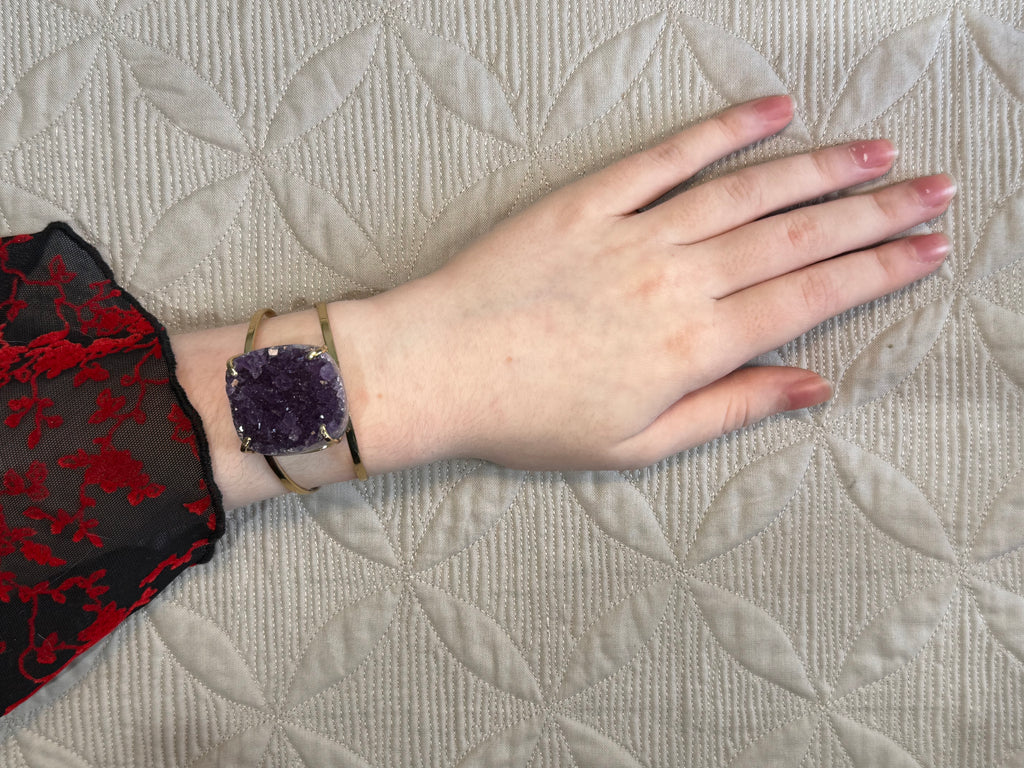 Hand wearing a purple crystal bracelet on a textured surface