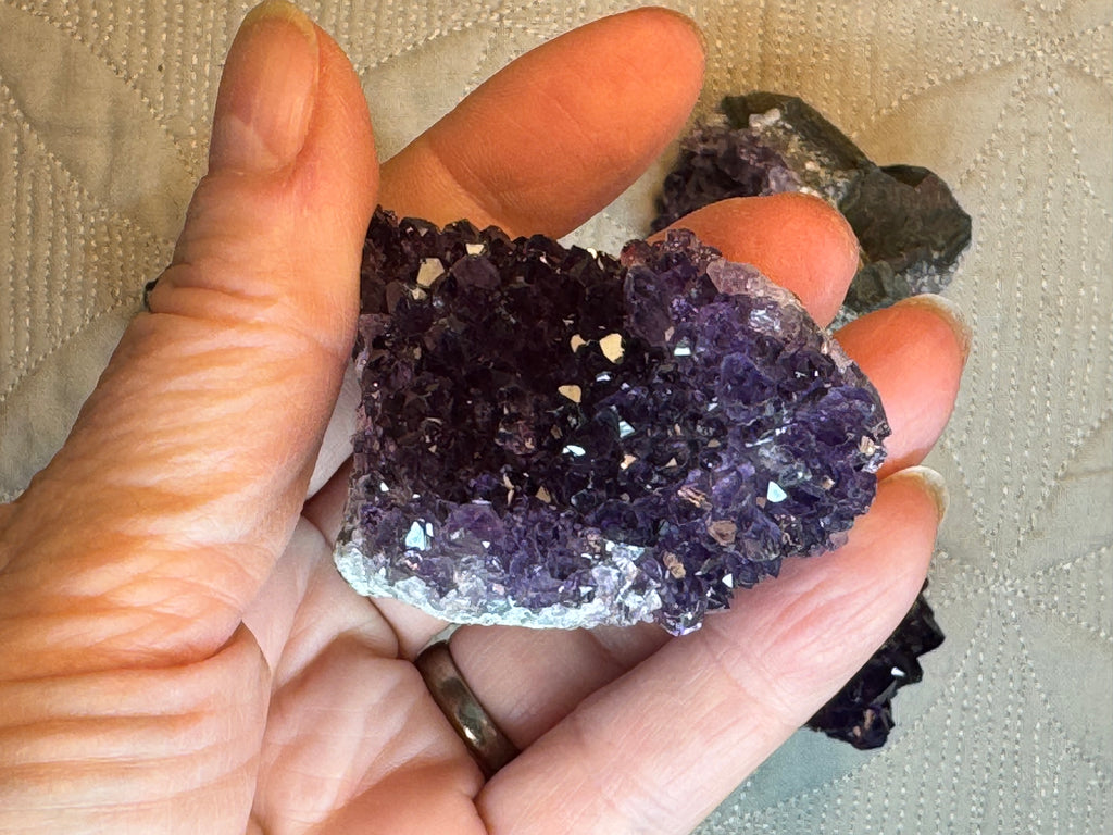 Hand holding a large amethyst crystal with smaller crystals in the background.