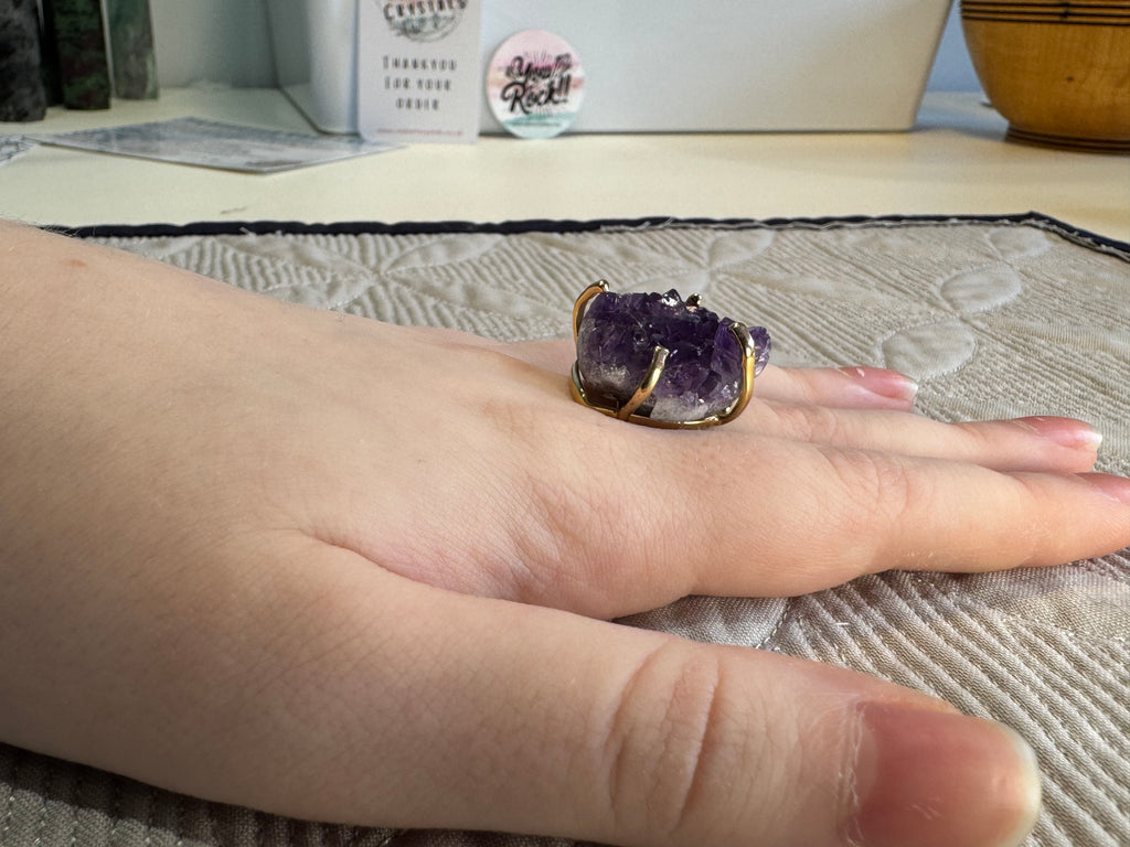 Hand wearing a purple amethyst ring on a textured surface with a blurred background