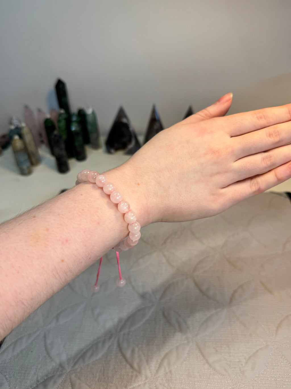 Hand wearing a pink beaded bracelet with a blurred background