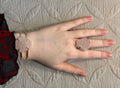Hand wearing a pink  rose quartznstone bracelet and ring on a textured surface