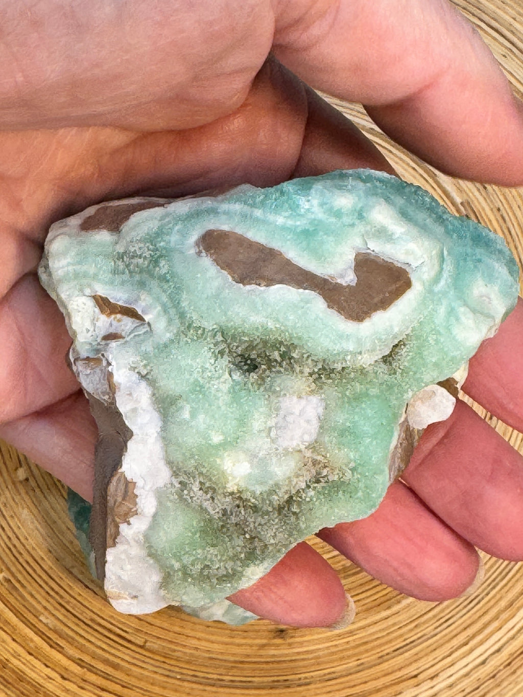 Hand holding a green and white mineral crystal on a wooden surface
