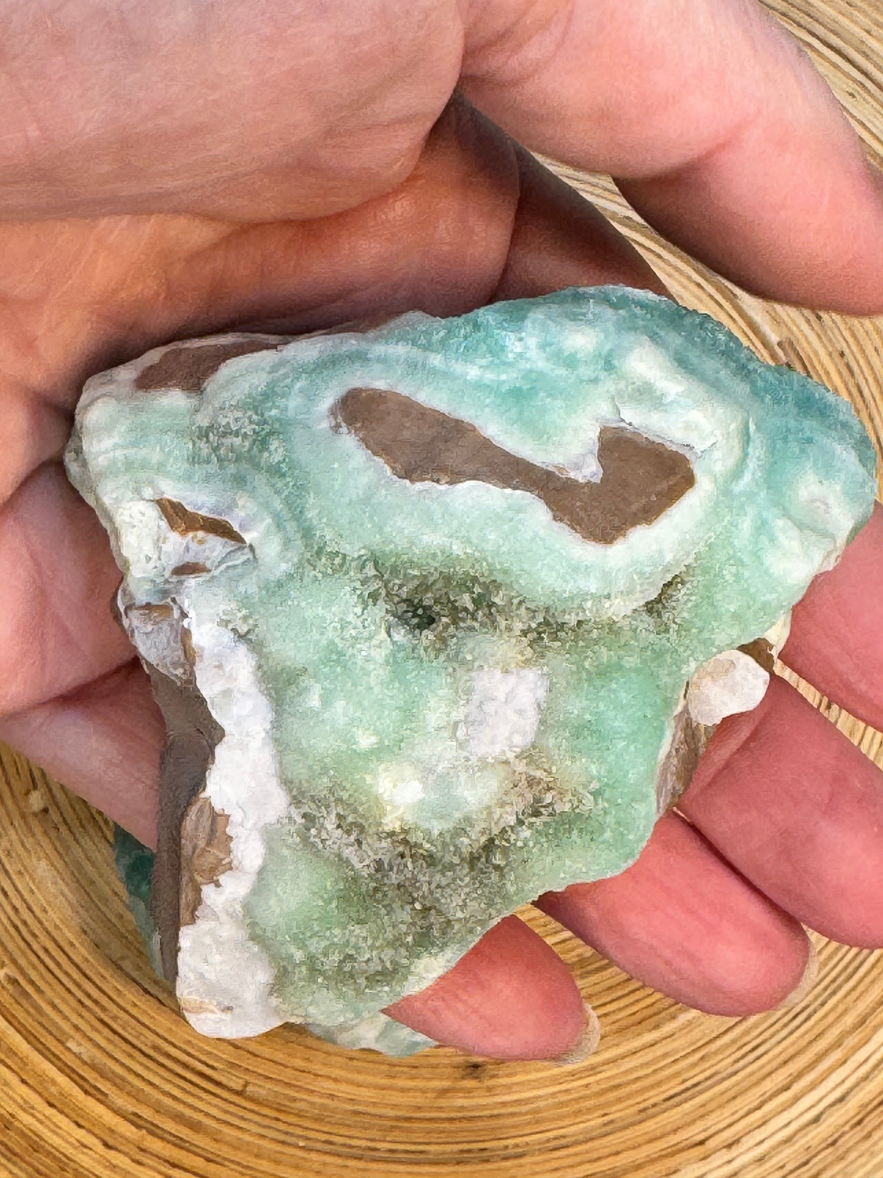 Hand holding a green and white mineral crystal on a wooden surface
