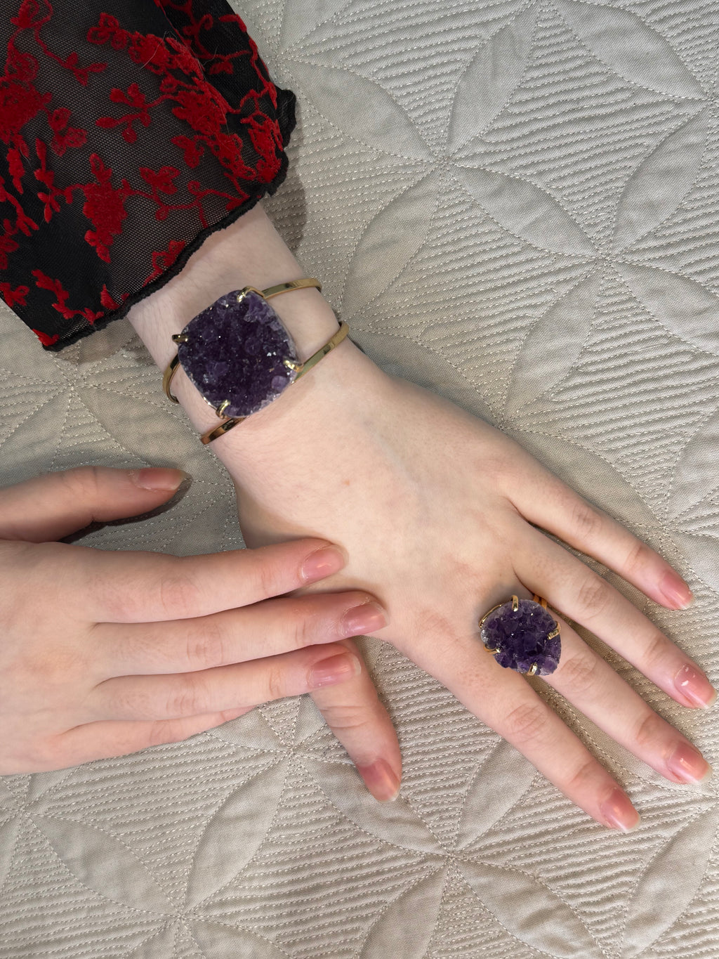 Hands wearing purple amethyst jewelry on a textured fabric background
