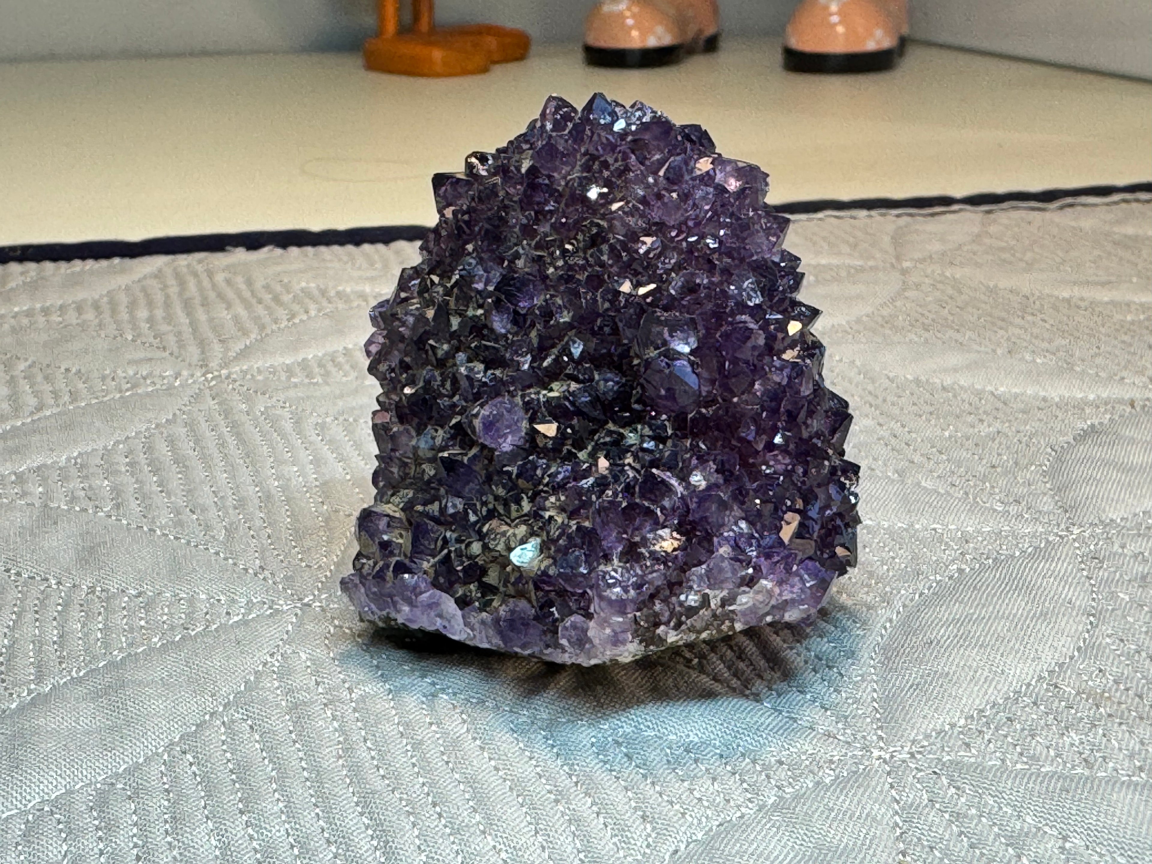 Amethyst crystal cluster on a textured surface with shoes in the background