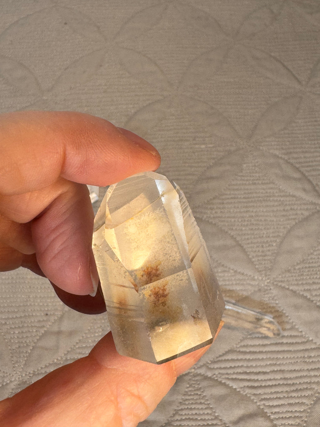 Clear crystal held in a hand against a textured gray background