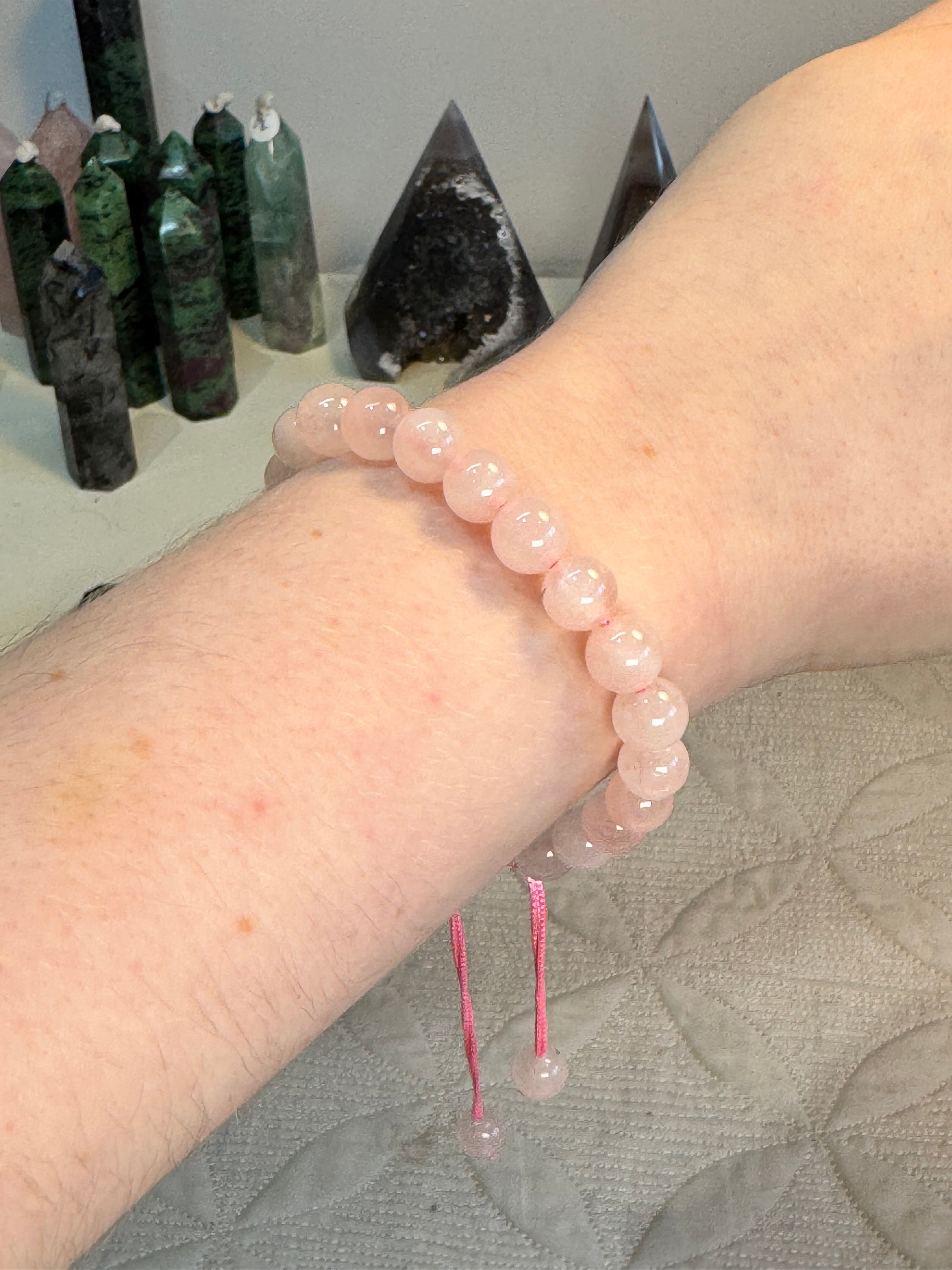 Person wearing a pink beaded bracelet with crystals in the background