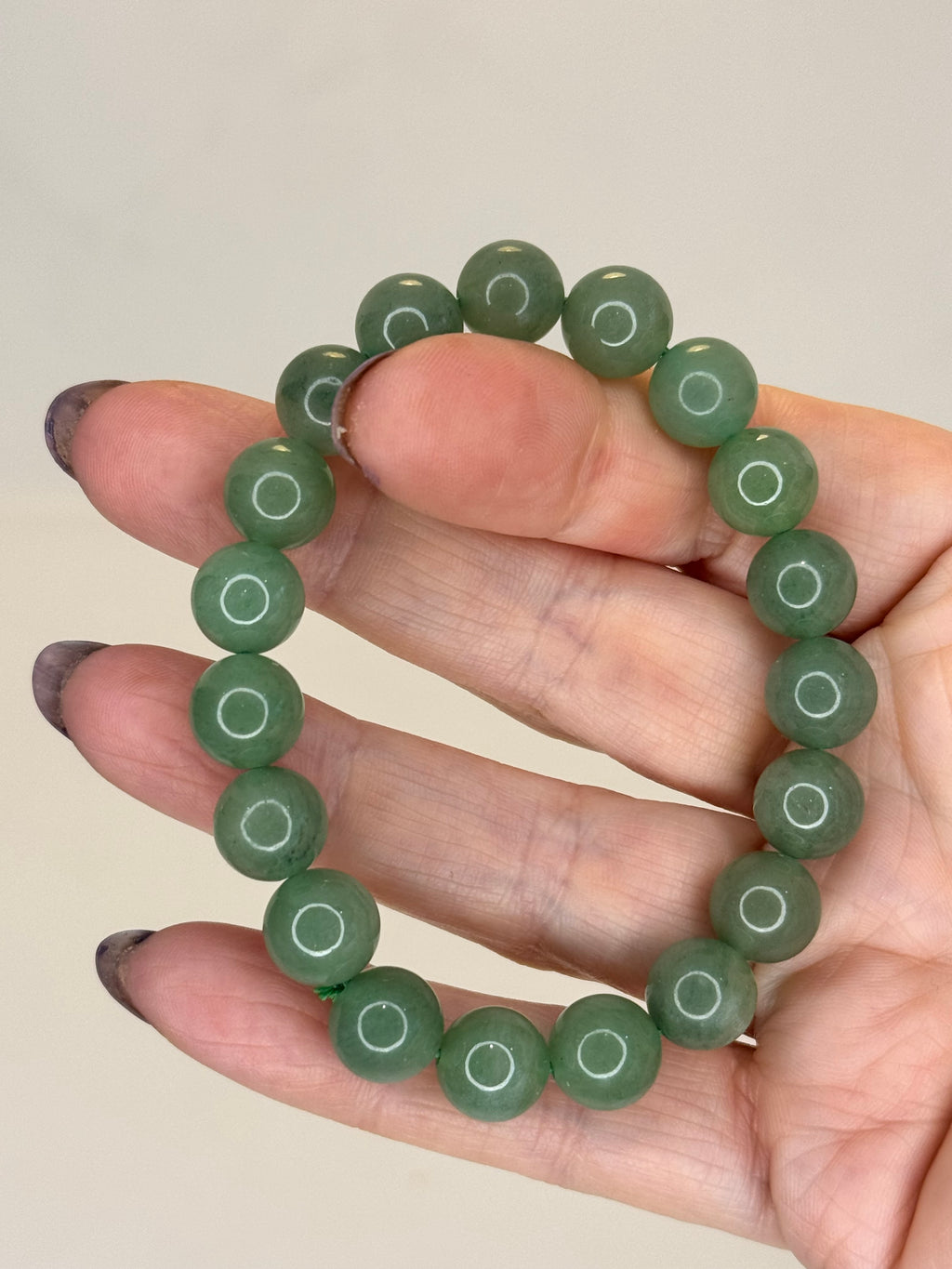 Green beaded bracelet on a hand against a beige background