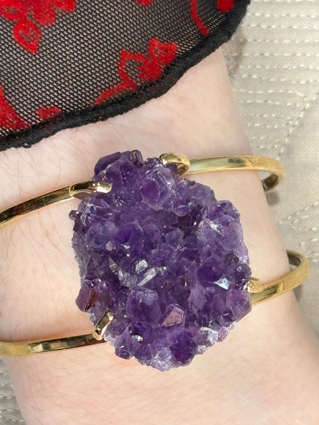 Gold bracelet with a large purple amethyst crystal on a wrist.