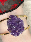 Gold bracelet with a large purple amethyst crystal on a wrist.