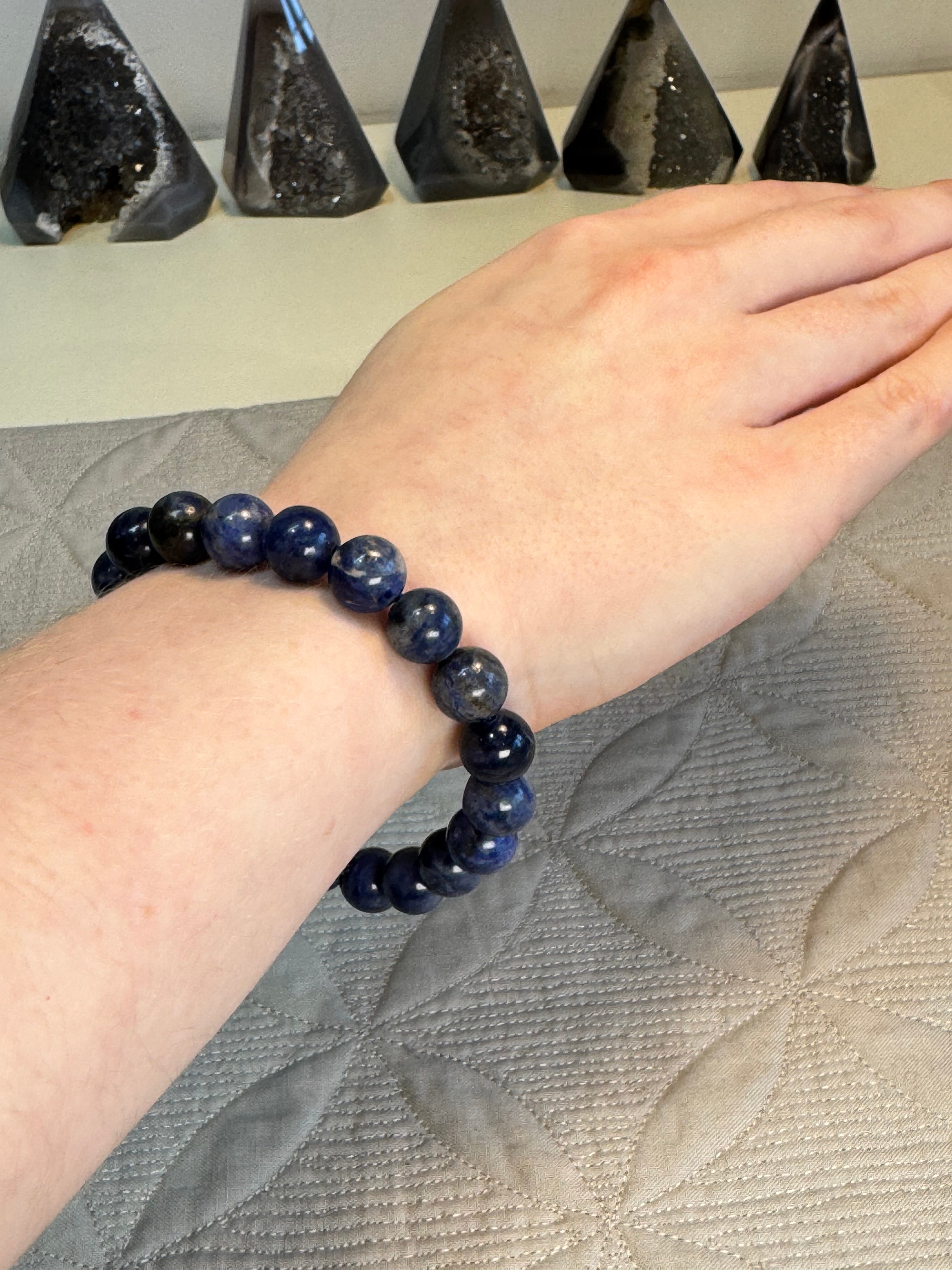 Hand wearing a blue beaded bracelet with a textured surface background