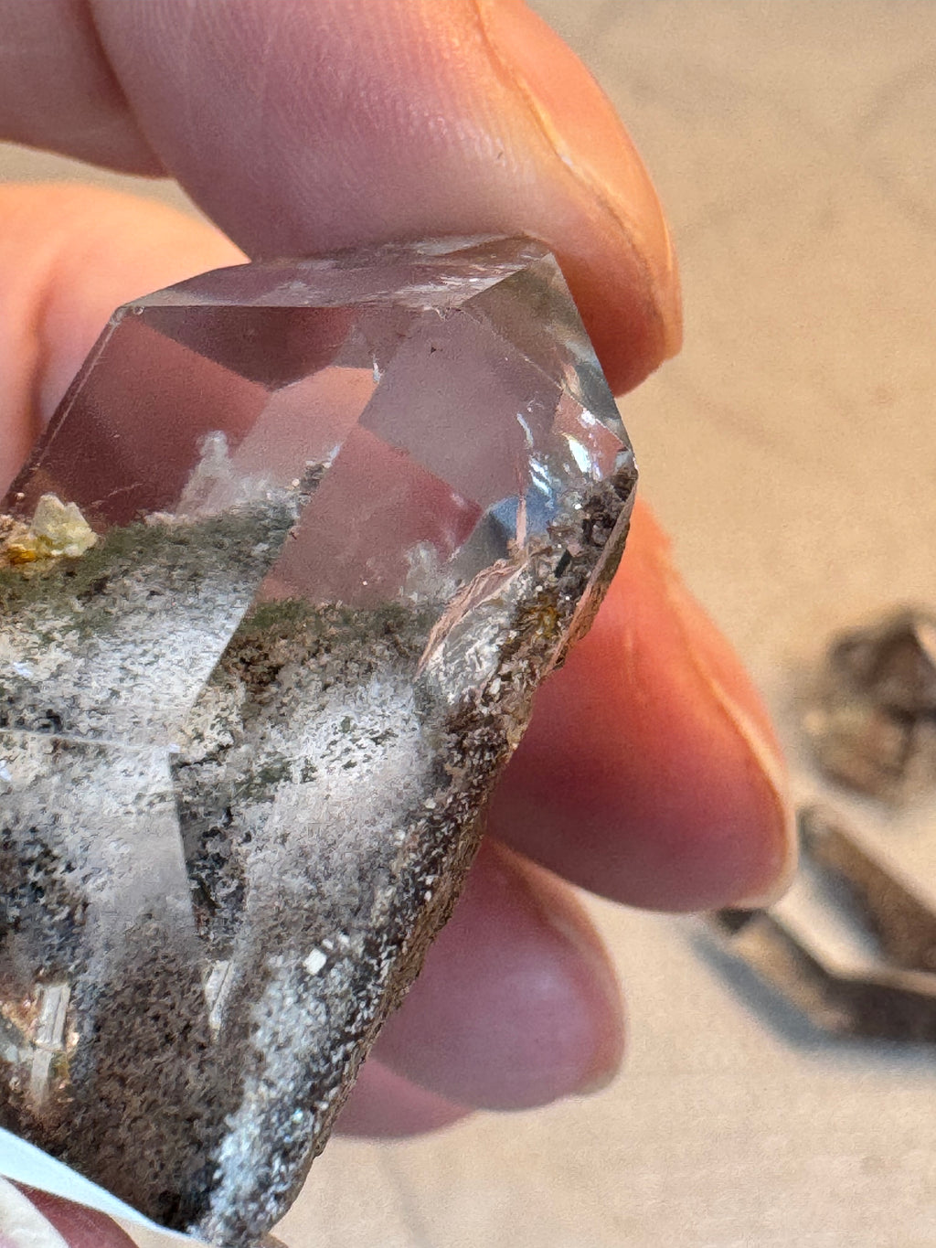 Clear crystal held between fingers with a blurred background
