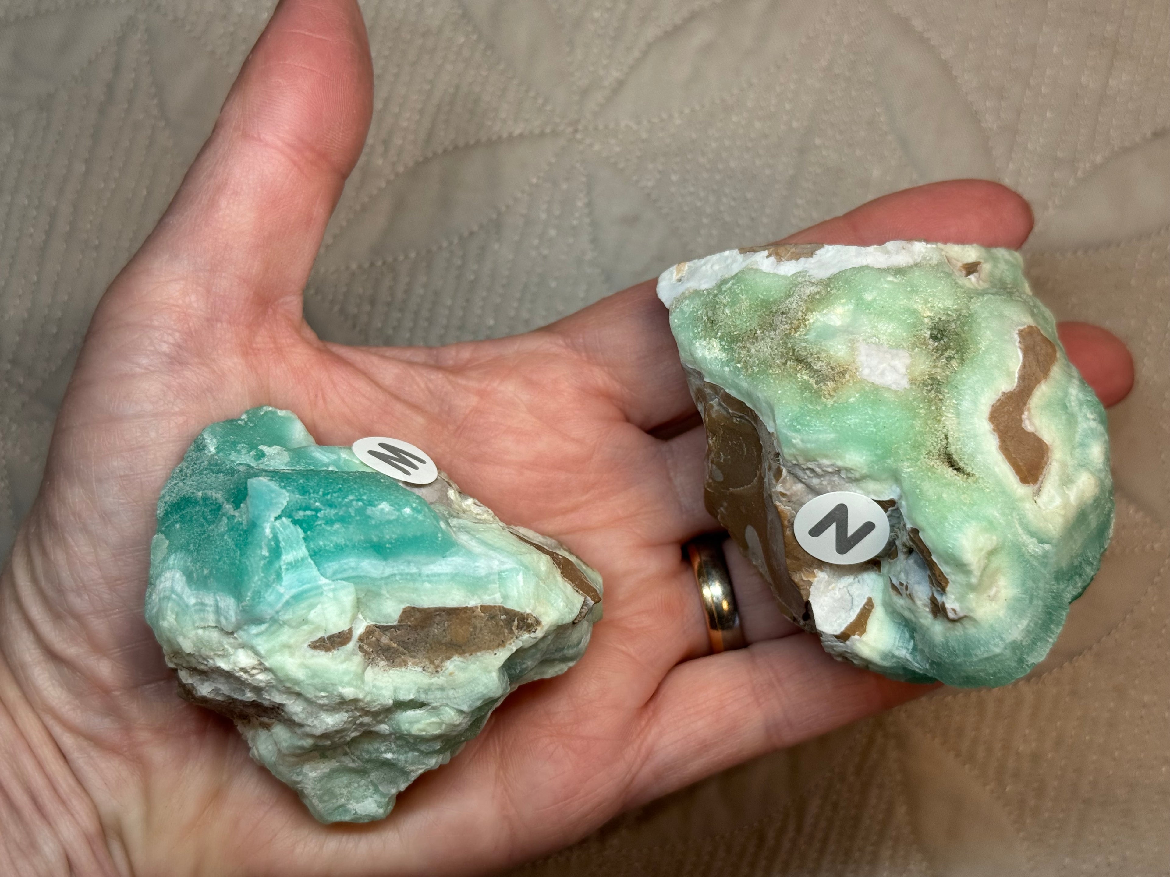 Two greenish crystals held in a hand against a beige background