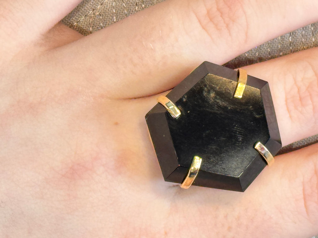Hexagonal black stone ring with gold accents on a finger