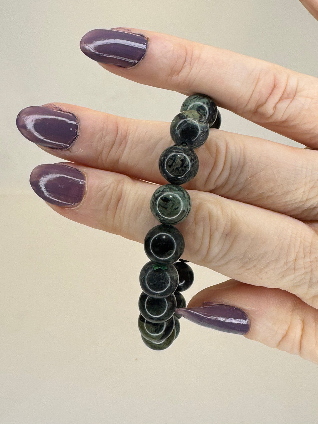Hand wearing a black beaded bracelet on a beige background