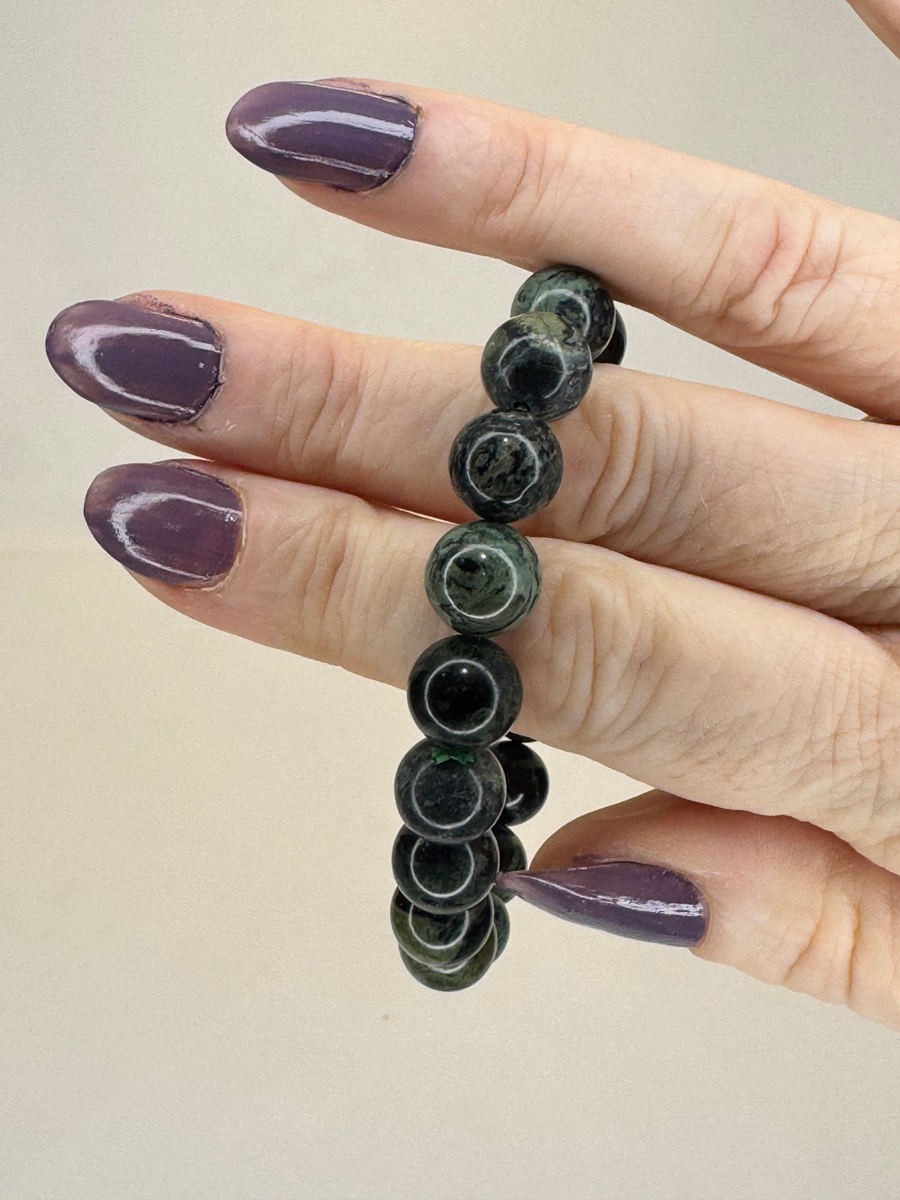 Hand wearing a black beaded bracelet on a beige background