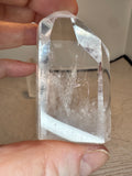 Clear crystal held between fingers against a neutral background