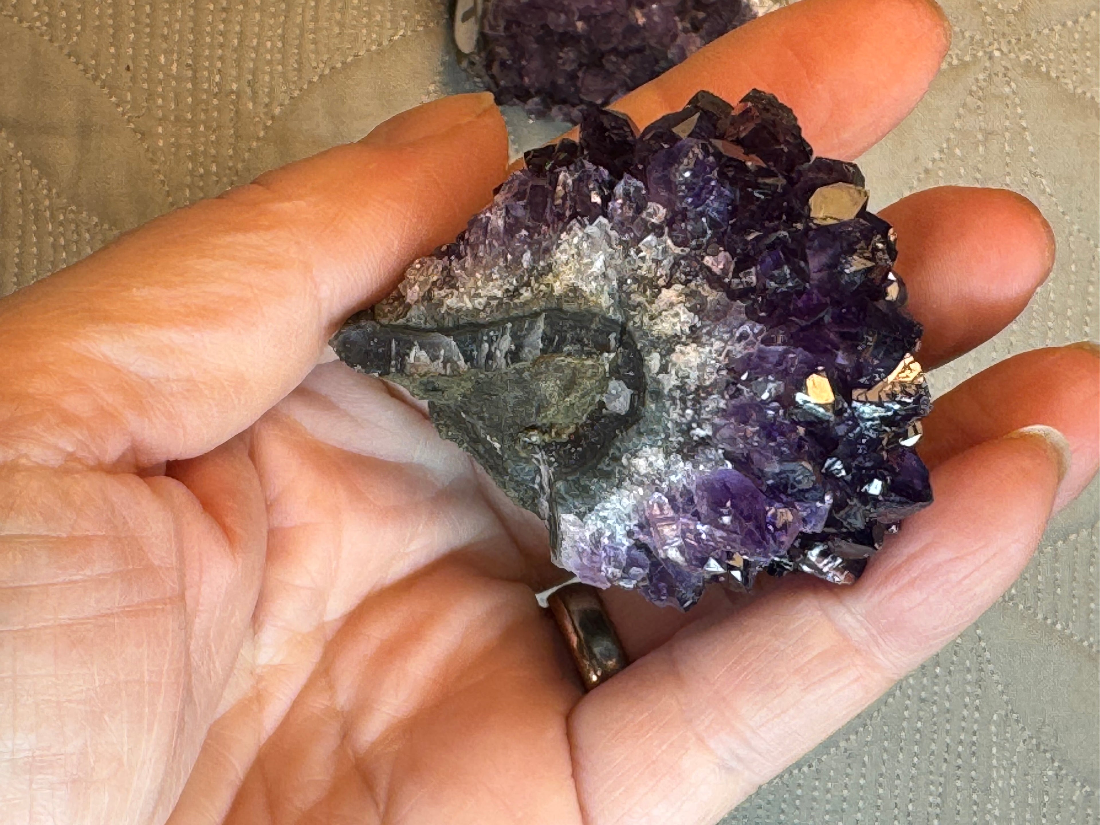 Hand holding a purple crystal cluster with a neutral background