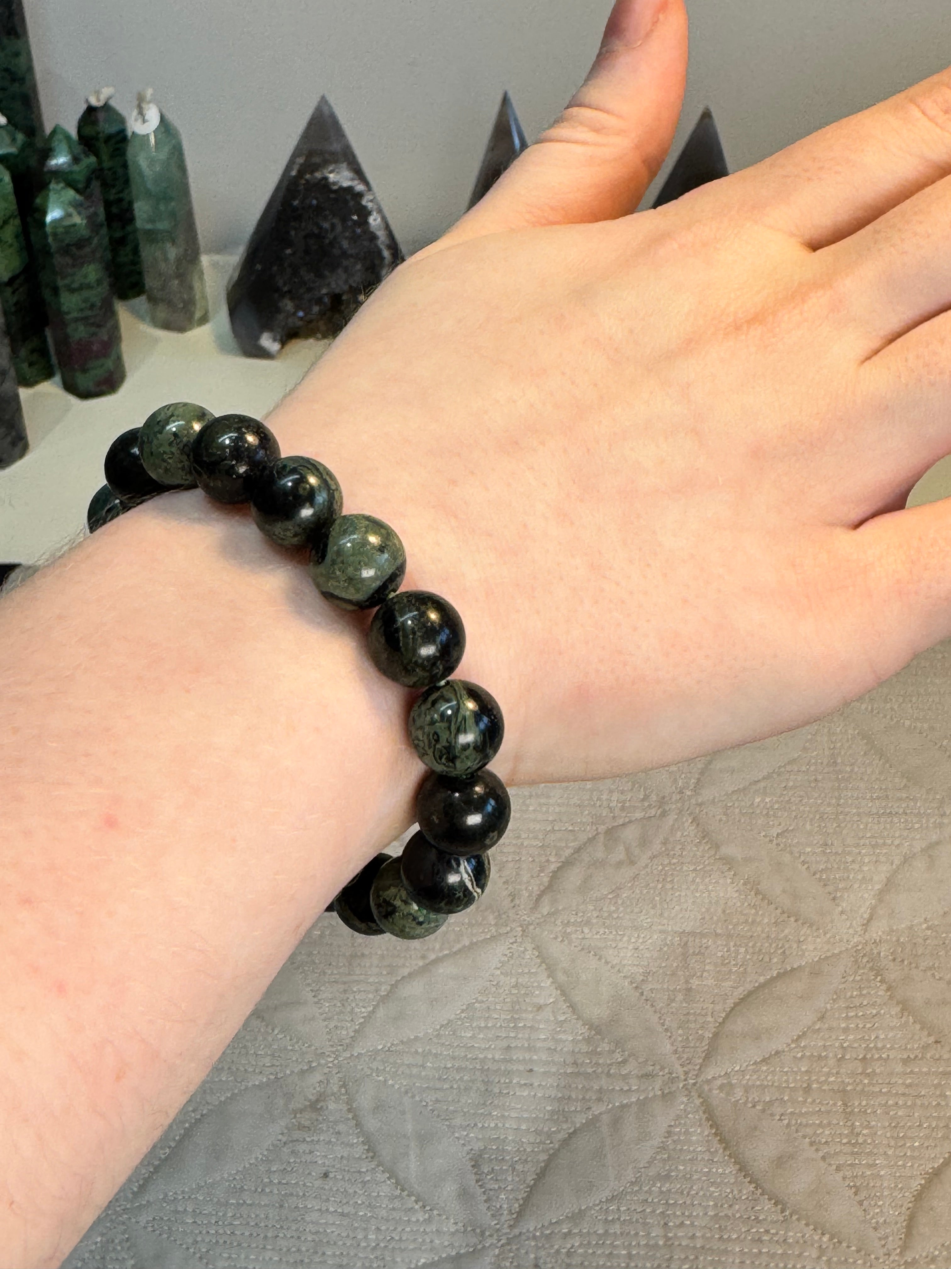 Hand wearing a green & black beaded bracelet with a textured surface background