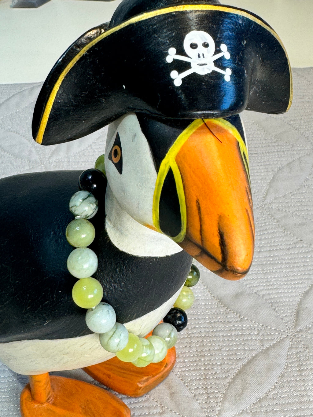 Puffin figurine wearing a pirate hat with a skull and crossbones, wearing a bracelet around its neck, on a textured white background