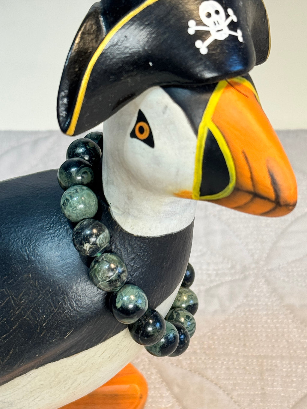 Puffin figurine wearing a pirate hat with a beaded kambala jasper bracelet on a white background