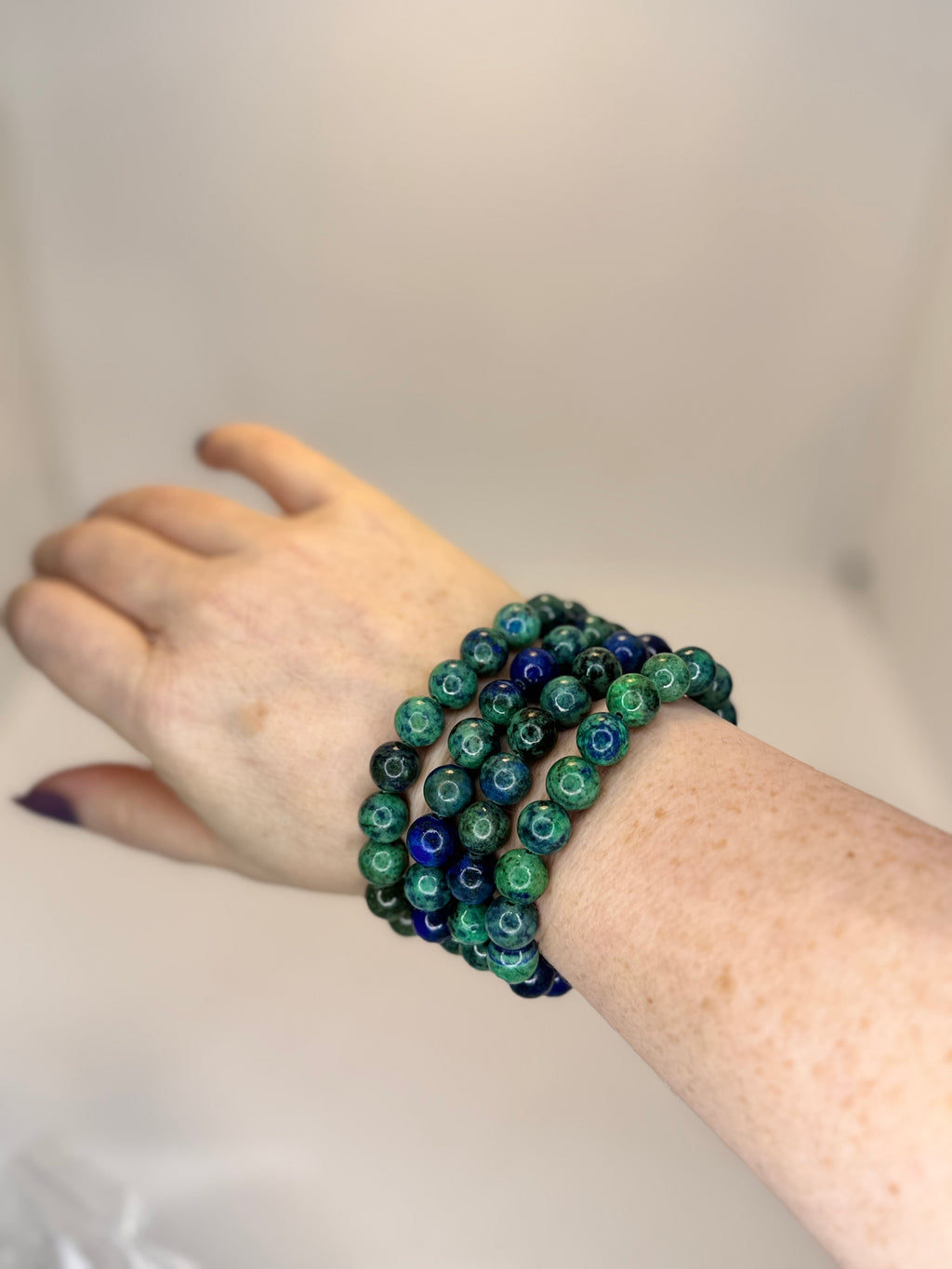 Hand wearing a stack of green and blue beaded bracelets on a plain background
