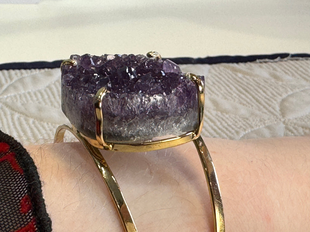 Gold bracelet with a large purple crystal on a textured surface