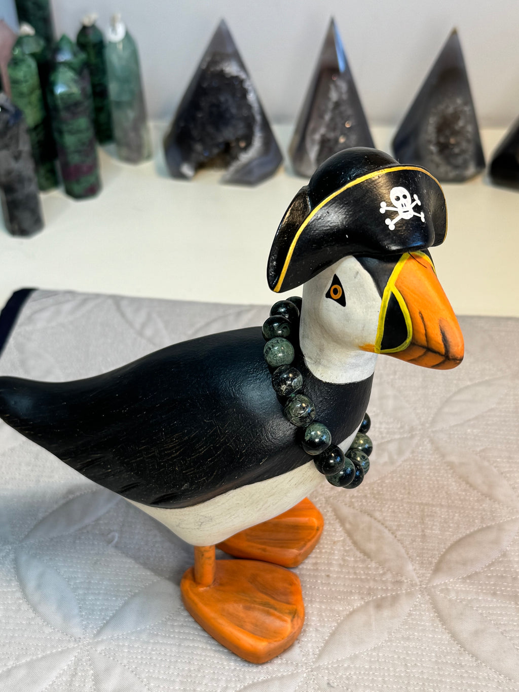 Puffin figurine wearing a pirate hat with a skull and crossbones on a textured white surface. with bracelet around its neck