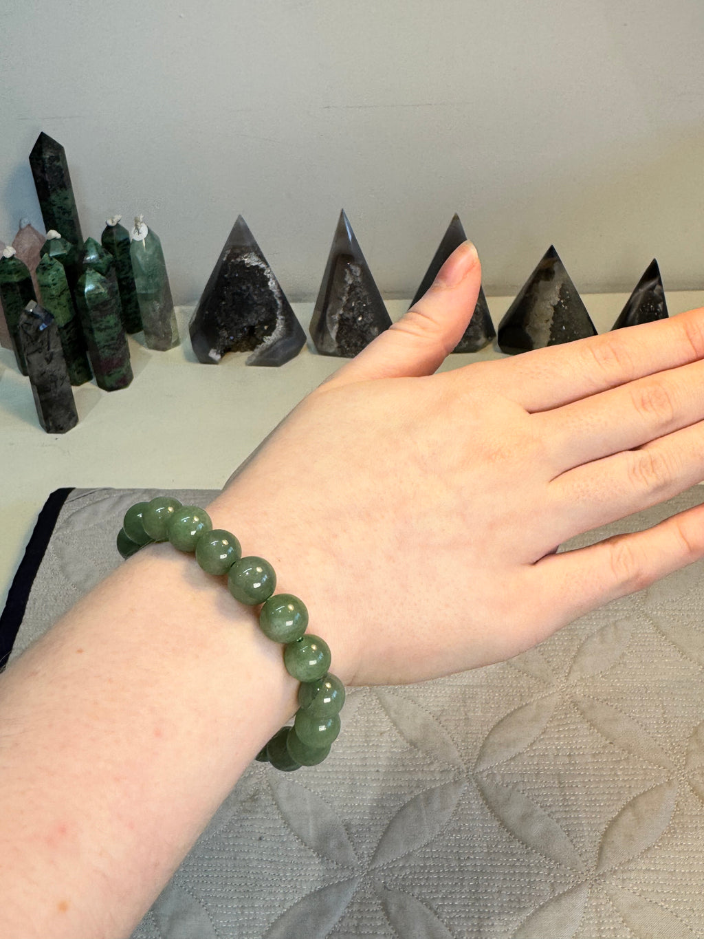 Hand wearing a green beaded bracelet with crystal points in the background