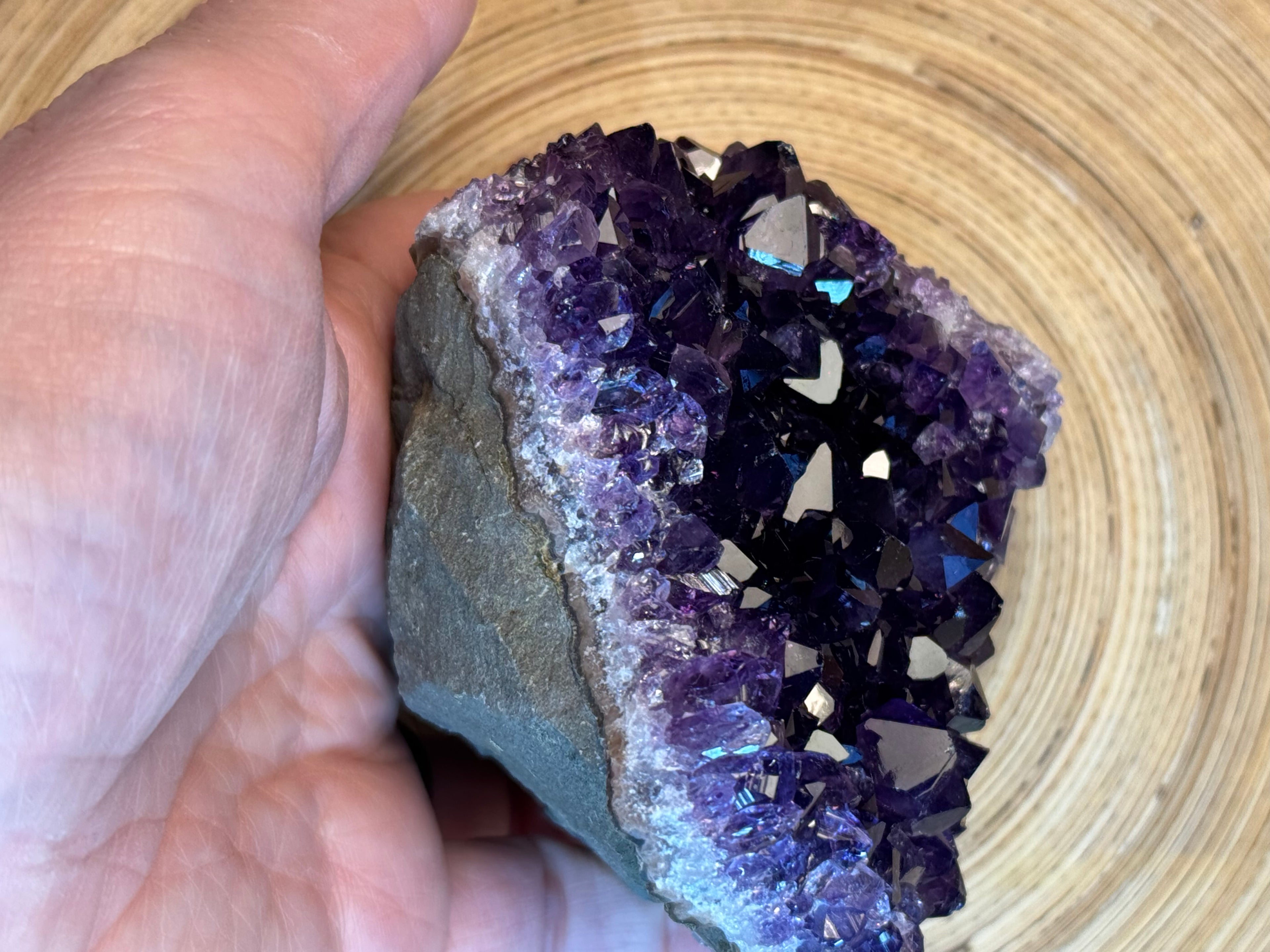 Amethyst crystal held by a hand against a woven basket background