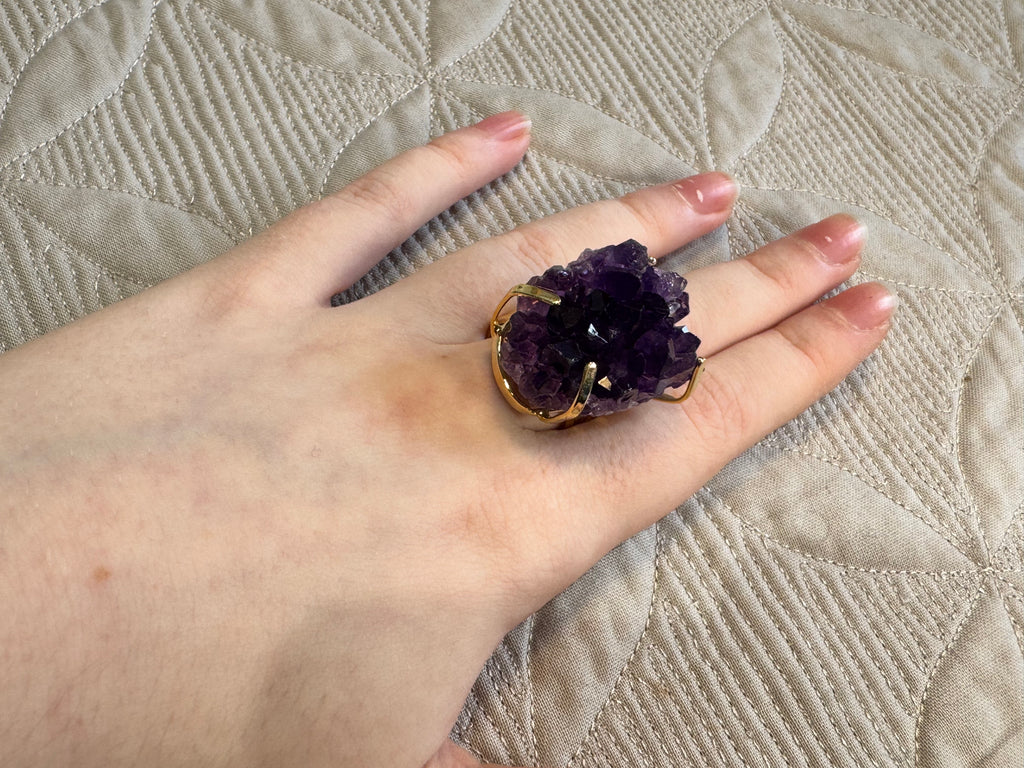 Hand wearing a purple amethyst ring on a textured surface