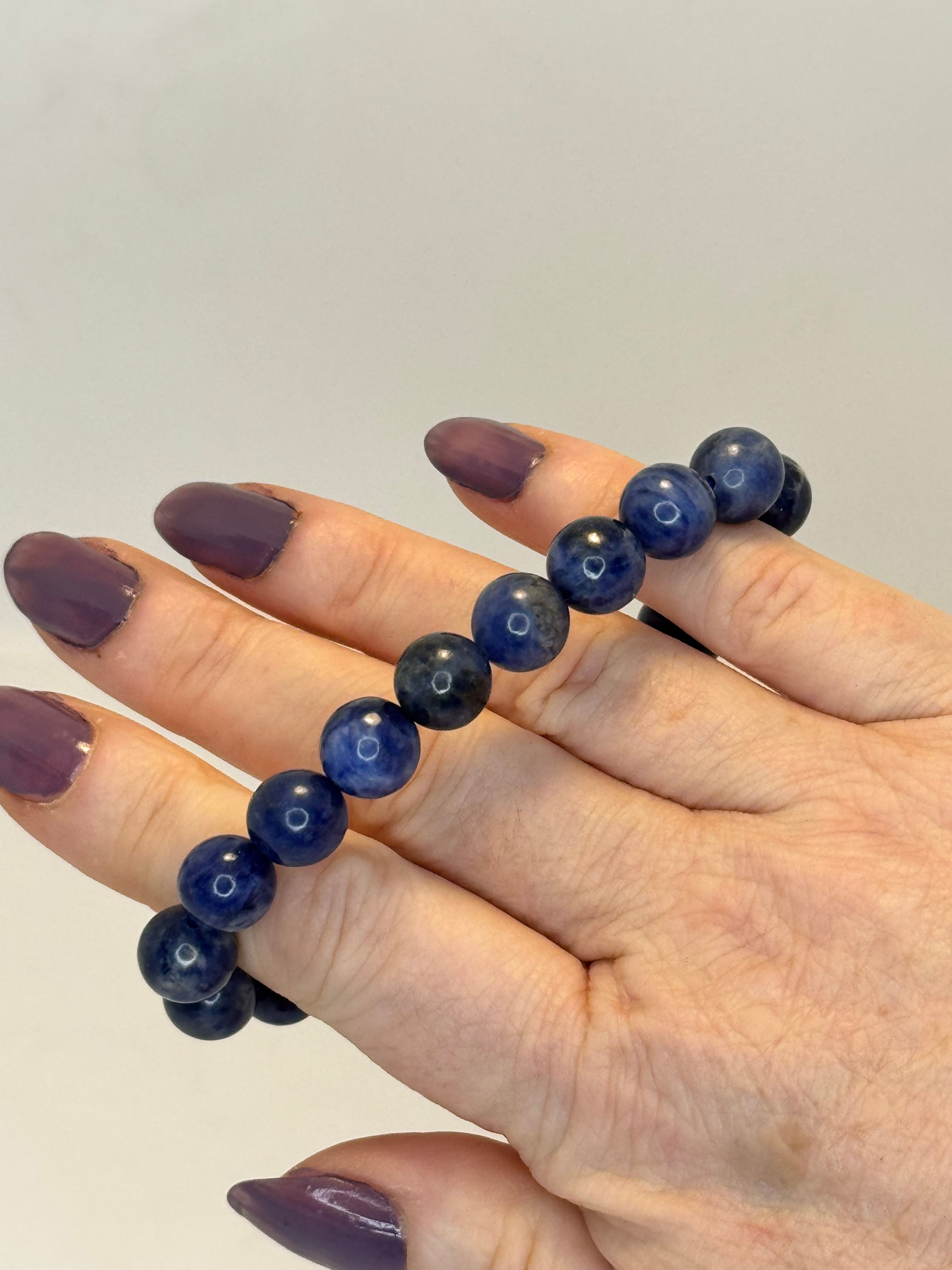 Hand wearing a blue beaded bracelet on a plain background