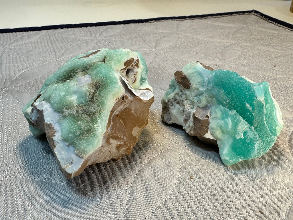 Two greenish-blue mineral specimens on a textured surface