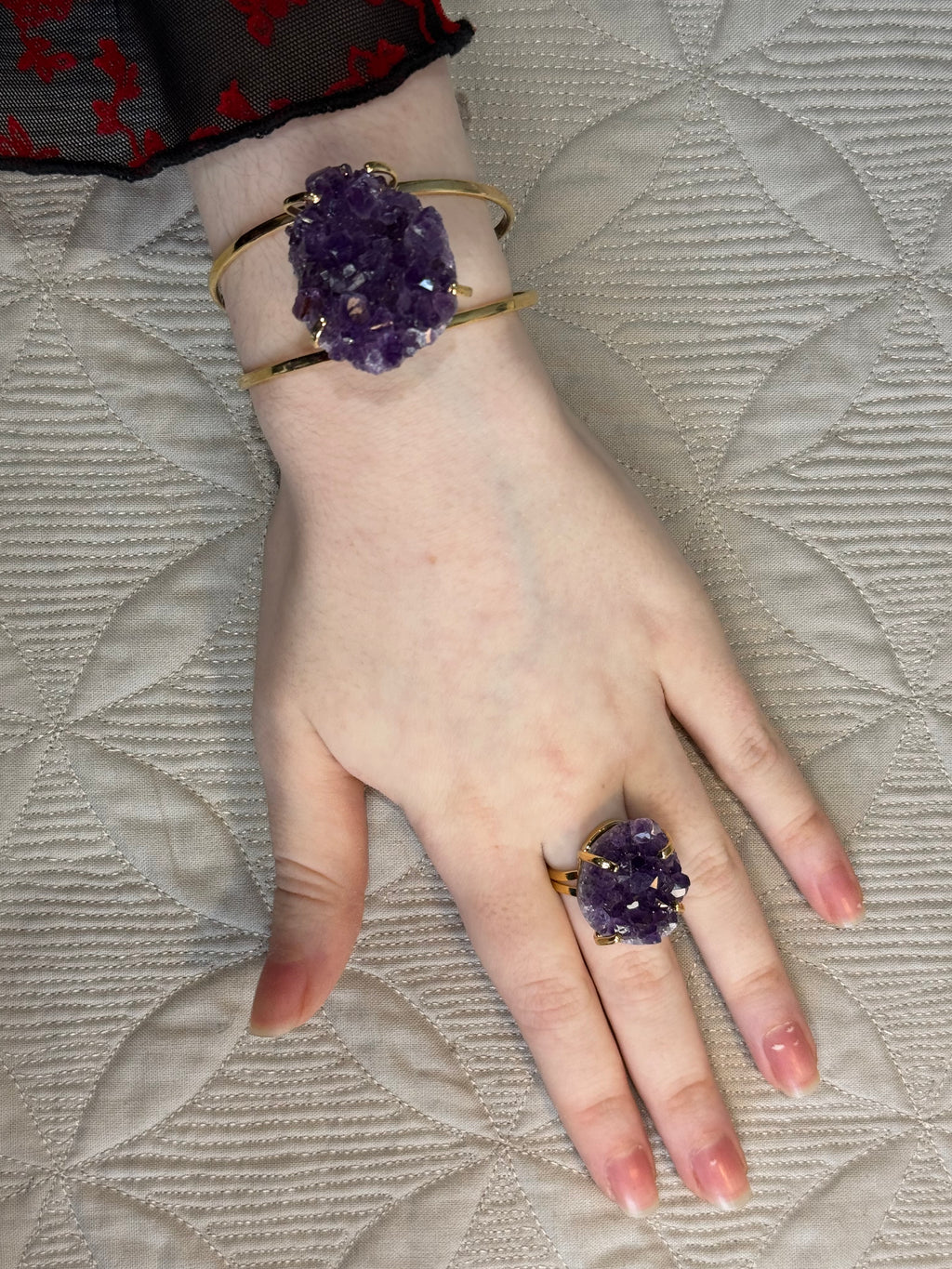 Hand wearing a purple amethyst ring and bracelet on a textured fabric background