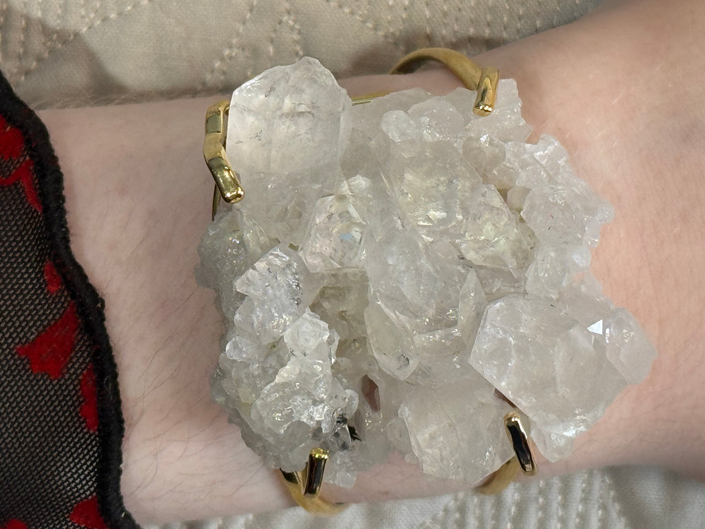 Hand holding a crystal cluster with gold bracelets on a textured background