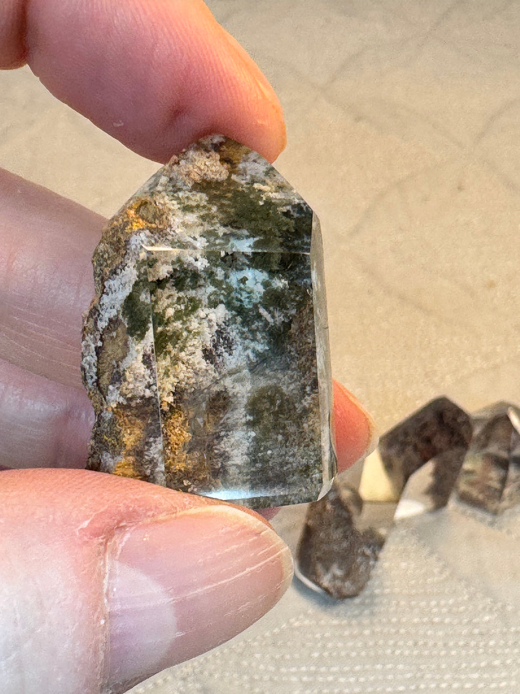 Person holding a rough crystal or mineral stone with a sandy background