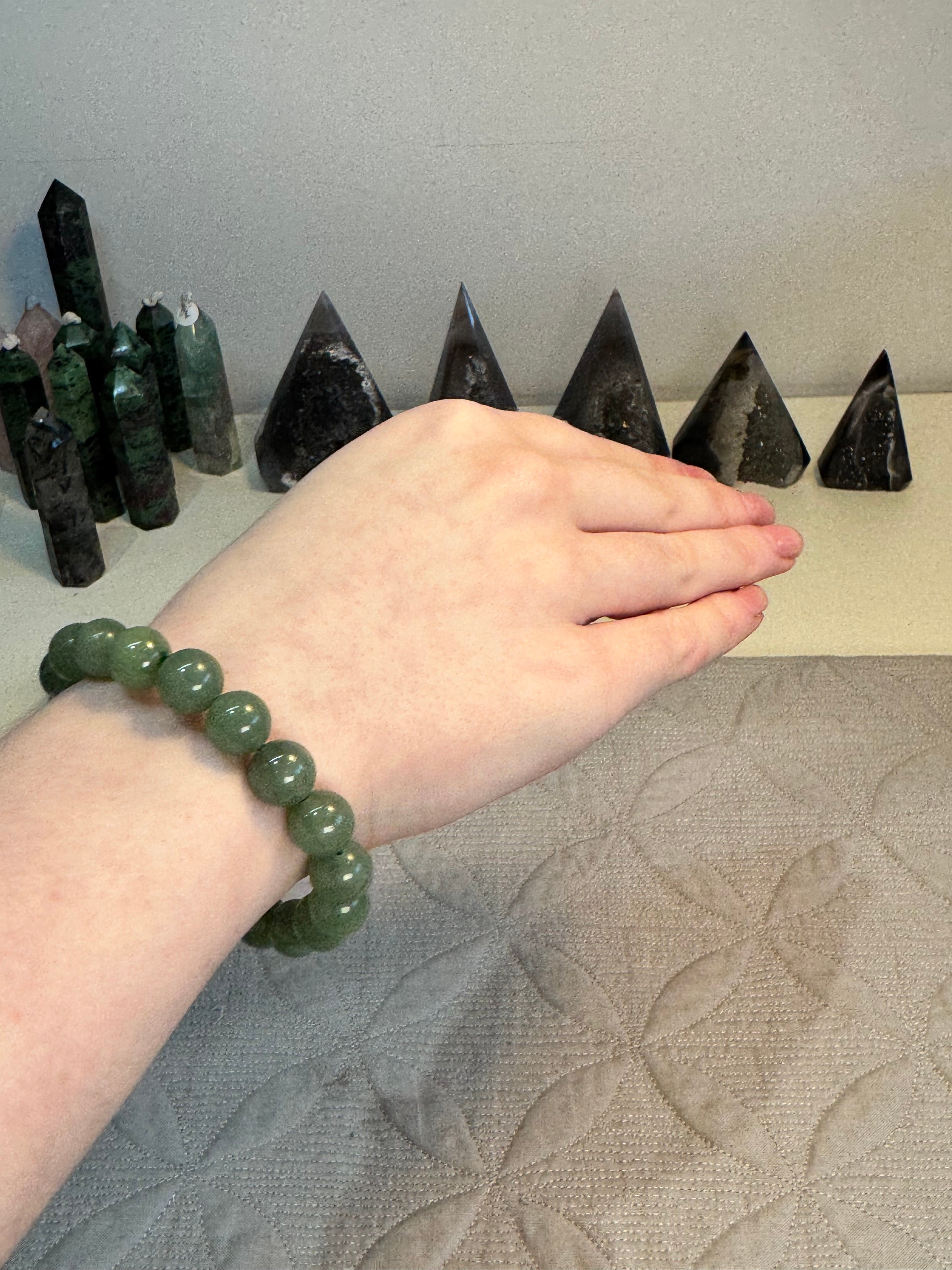 Hand with a green beaded bracelet resting on a pyramid-shaped crystal structure.